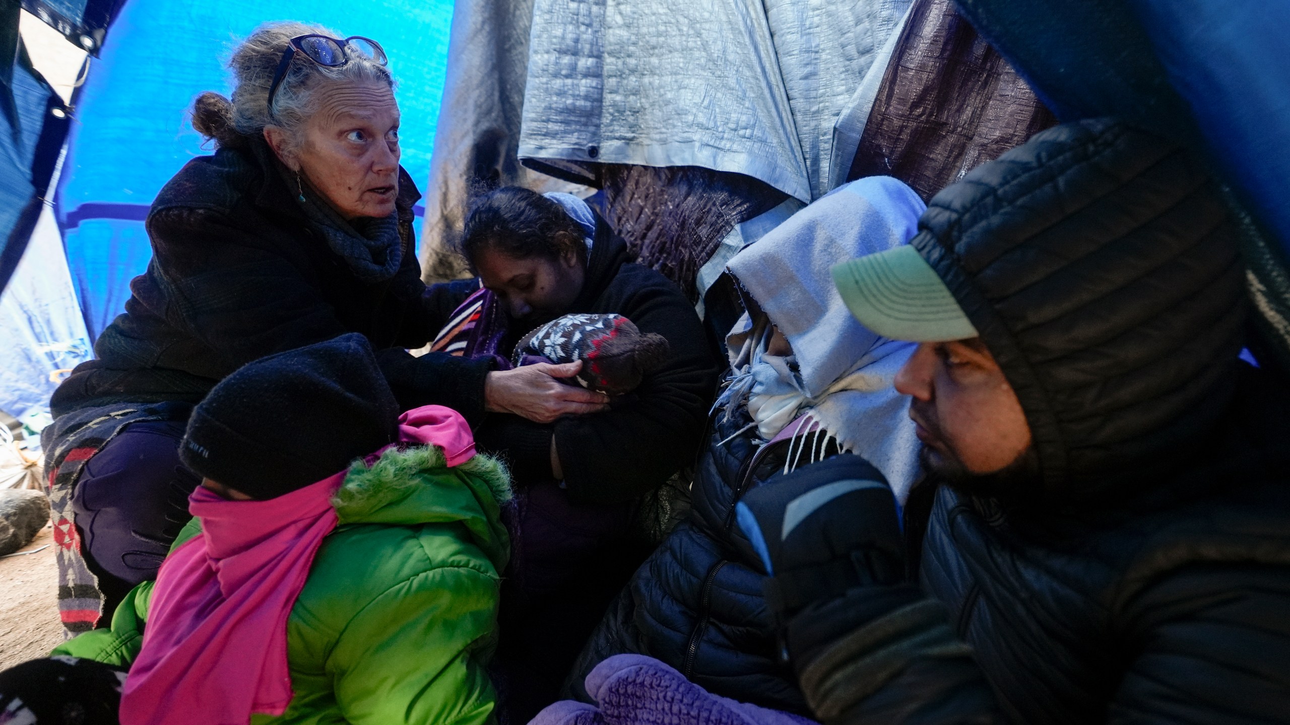 FILE - Medical volunteer Karen Parker, left, touches a 2-year-old child with a fever as she talks to a family of asylum-seeking migrants as they wait to be processed in a makeshift, mountainous campsite after crossing the border with Mexico, Feb. 2, 2024, near Jacumba Hot Springs, Calif. A federal judge on Friday, March 29, sharply questioned the Biden administration's position that it bears no responsibility for housing and feeding migrant children while they wait in makeshift camps along the U.S-Mexico border. (AP Photo/Gregory Bull, File)