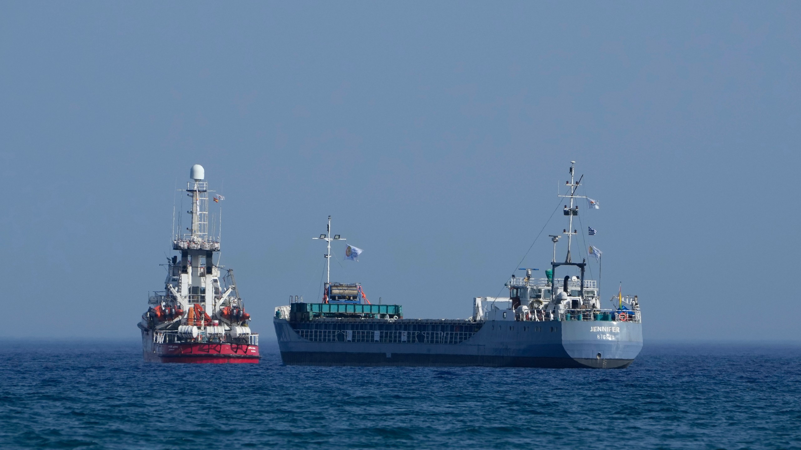 A cargo ship, right, and a ship belonging to the Open Arms aid group, are loaded with 240 tons of canned food destined for Gaza prepare to set sail outside the Cypriot port of Larnaca, Cyprus, on Saturday, March 30, 2024. U.S. charity World Central Kitchen says the ship, named Jennifer, was due to depart following the inaugural voyage of the Cyprus-Gaza sea route earlier this month by the Open Arms vessel that delivered 200 tons of food and water. (AP Photo/Petros Karadjias)