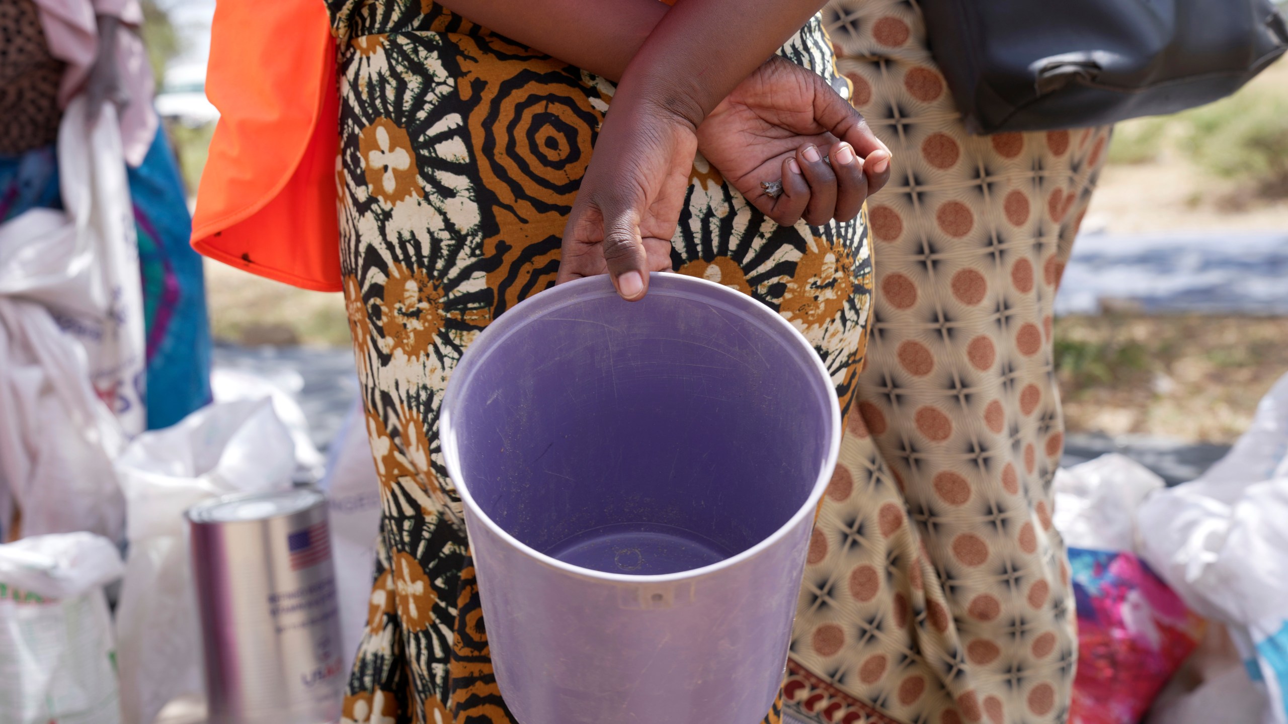 A woman holds an empty bucket while waiting to receive food aid in a queue in Mangwe district in southwestern Zimbabwe, Friday, March, 22, 2024. A new drought has left millions facing hunger in southern Africa as they experience the effects of extreme weather that scientists say is becoming more frequent and more damaging. (AP Photo/Tsvangirayi Mukwazhi)