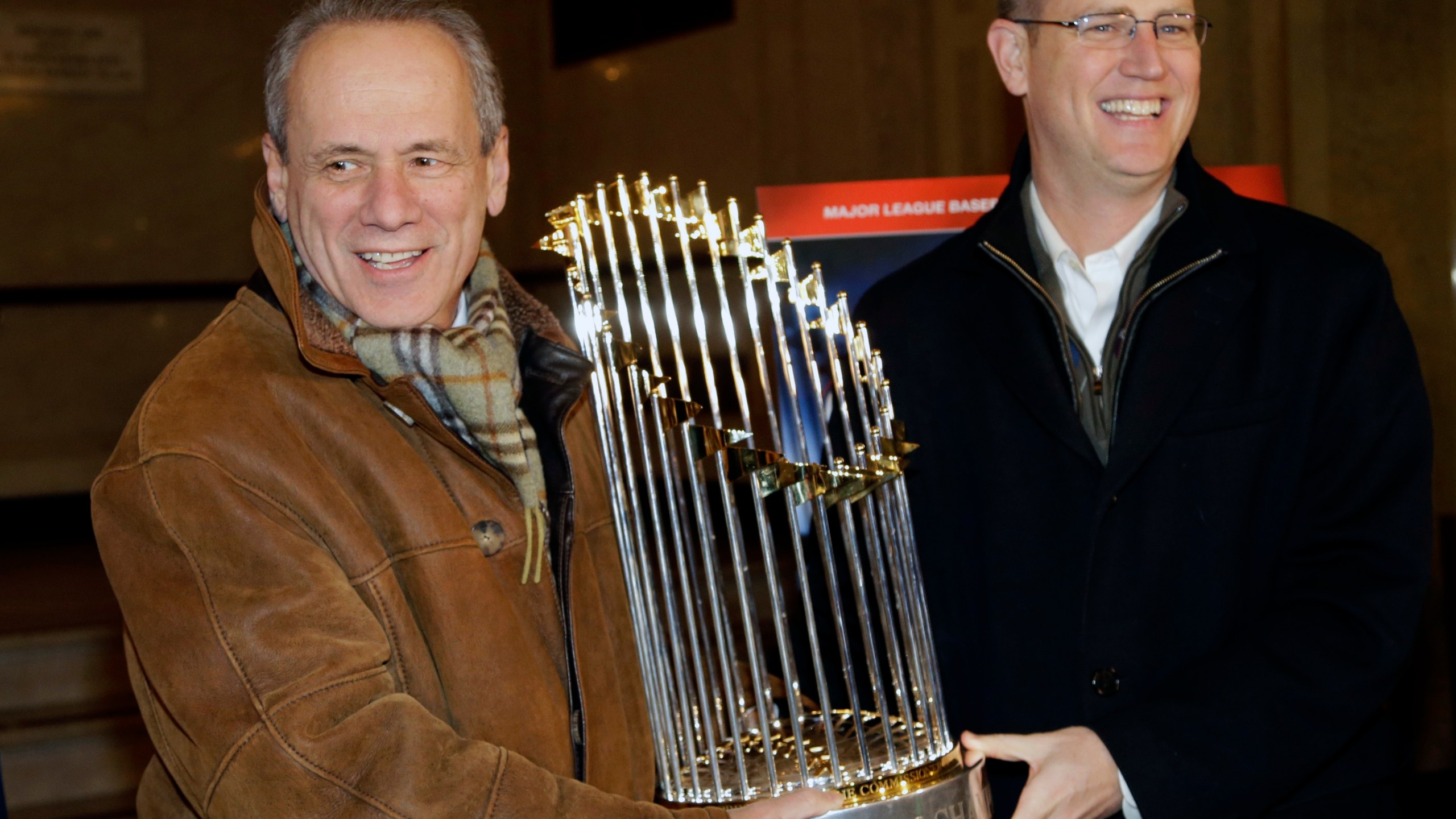 FILE -FILE - Boston Red Sox CEO Larry Lucchino, left, and Chief Operating Officer Sam Kennedy hold the 2013 World Series baseball trophy on the red carpet at the Wang Theatre before a screening of a DVD about the series in Boston., Nov. 23, 2013. Larry Lucchino, the force behind baseball’s retro ballpark revolution and the transformation of the Boston Red Sox from cursed losers to World Series champions, has died. He was 78. Lucchino had suffered from cancer. The Triple-A Worcester Red Sox, his last project in a career that also included three major league baseball franchises and one in the NFL, confirmed his death on Tuesday, April 2, 2024. (AP Photo/Steven Senne, File)
