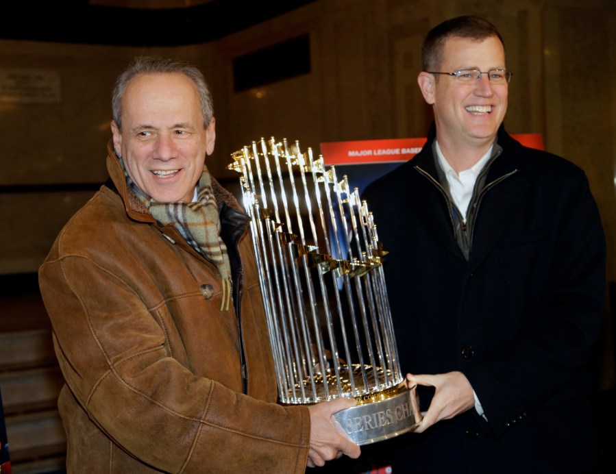 FILE -FILE - Boston Red Sox CEO Larry Lucchino, left, and Chief Operating Officer Sam Kennedy hold the 2013 World Series baseball trophy on the red carpet at the Wang Theatre before a screening of a DVD about the series in Boston., Nov. 23, 2013. Larry Lucchino, the force behind baseball’s retro ballpark revolution and the transformation of the Boston Red Sox from cursed losers to World Series champions, has died. He was 78. Lucchino had suffered from cancer. The Triple-A Worcester Red Sox, his last project in a career that also included three major league baseball franchises and one in the NFL, confirmed his death on Tuesday, April 2, 2024. (AP Photo/Steven Senne, File)