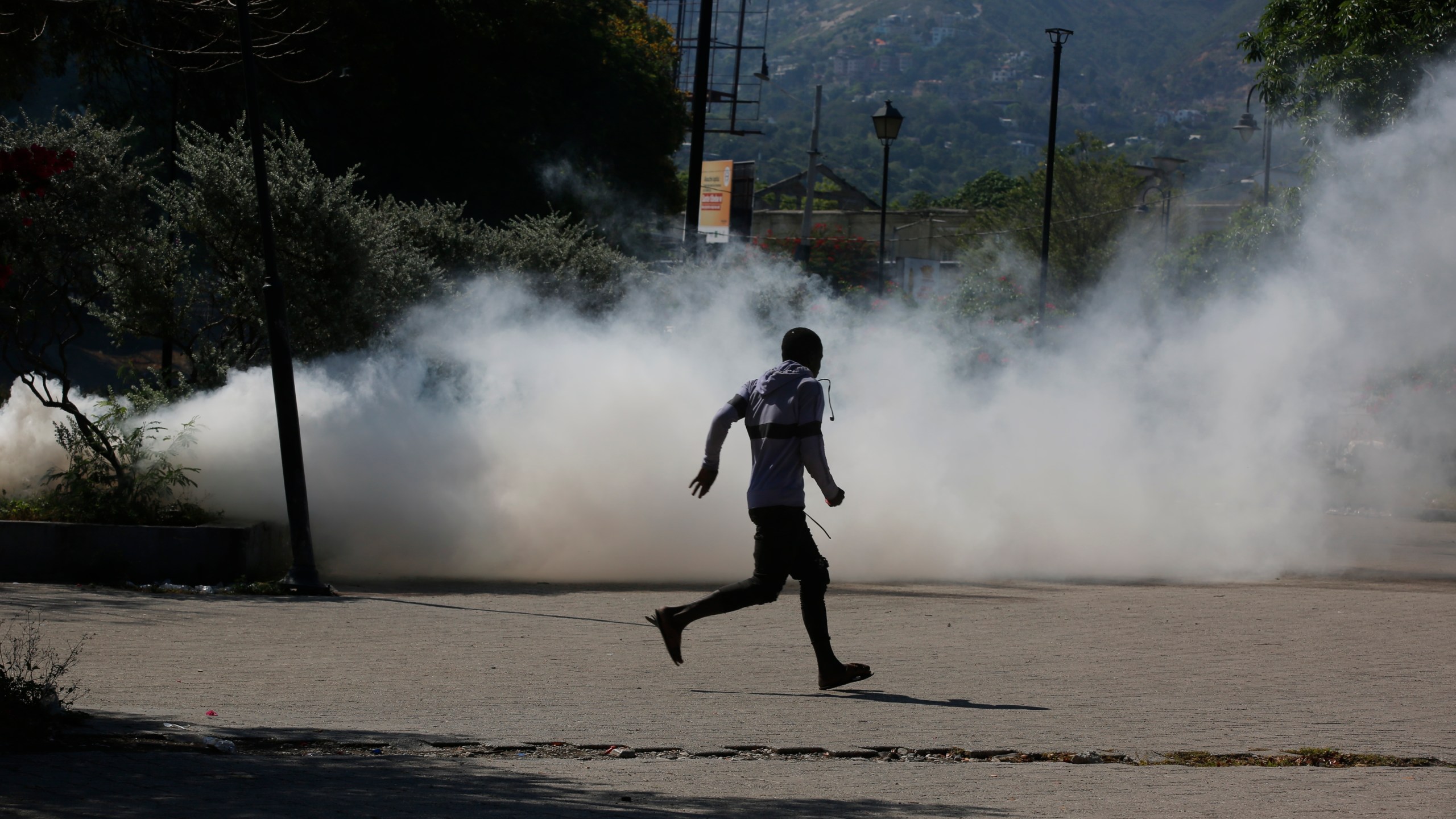A man runs for cover as riot police launch tear gas in an effort to remove street vendors in the Champs de Mars area, next to the National Palace, in Port-au-Prince, Haiti, Tuesday, April 2, 2024. (AP Photo/Odelyn Joseph)