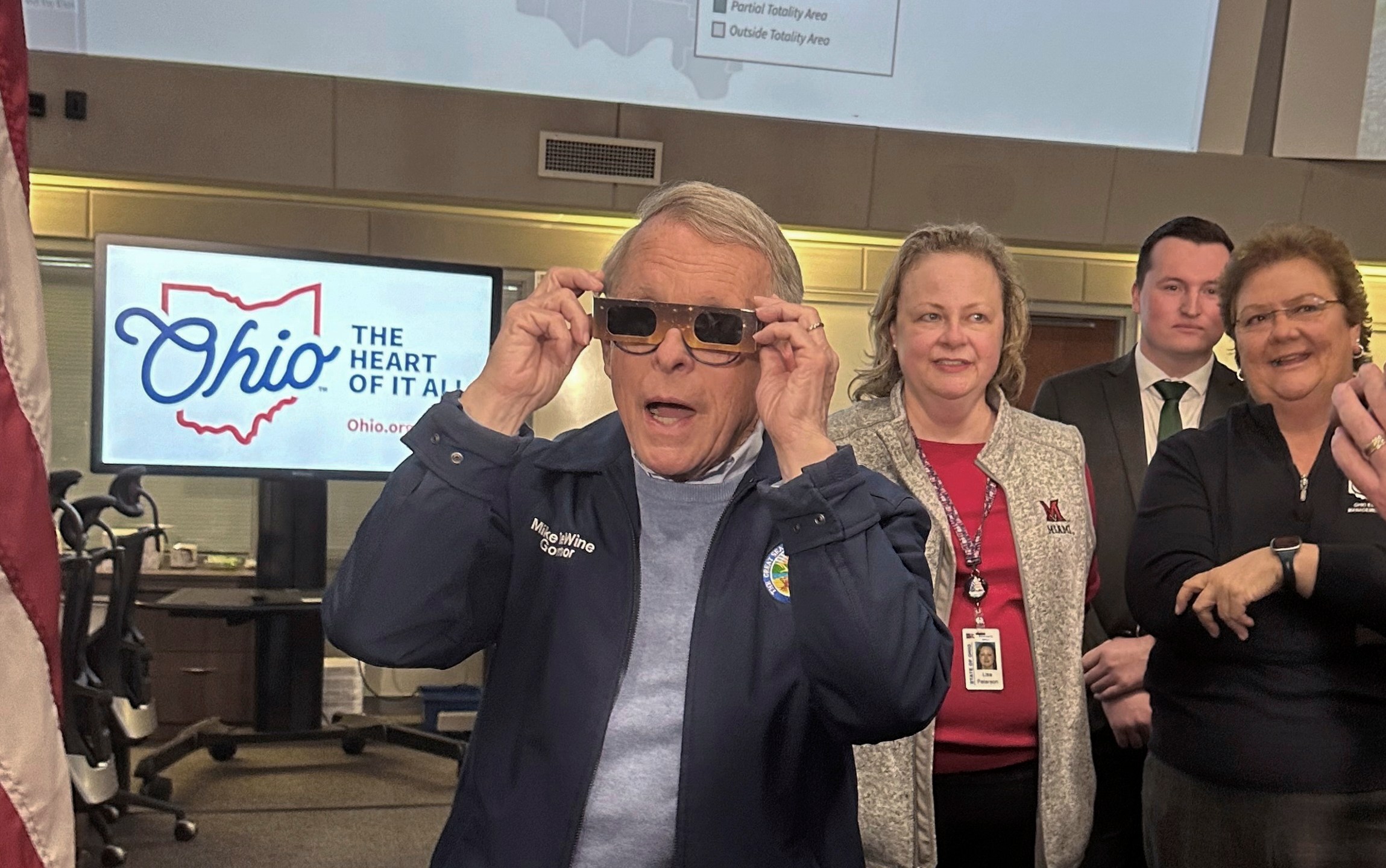 Republican Ohio Gov. Mike DeWine sports a pair of eclipse glasses while talking to reporters at the Ohio Emergency Operations Center in Columbus, Ohio, on Friday, April 5, 2024. DeWine activated the center on Friday to assist communities before, during and after Monday's total solar eclipse, which could draw hundreds of thousands of tourists to the state. (AP Photo/Julie Carr Smyth)