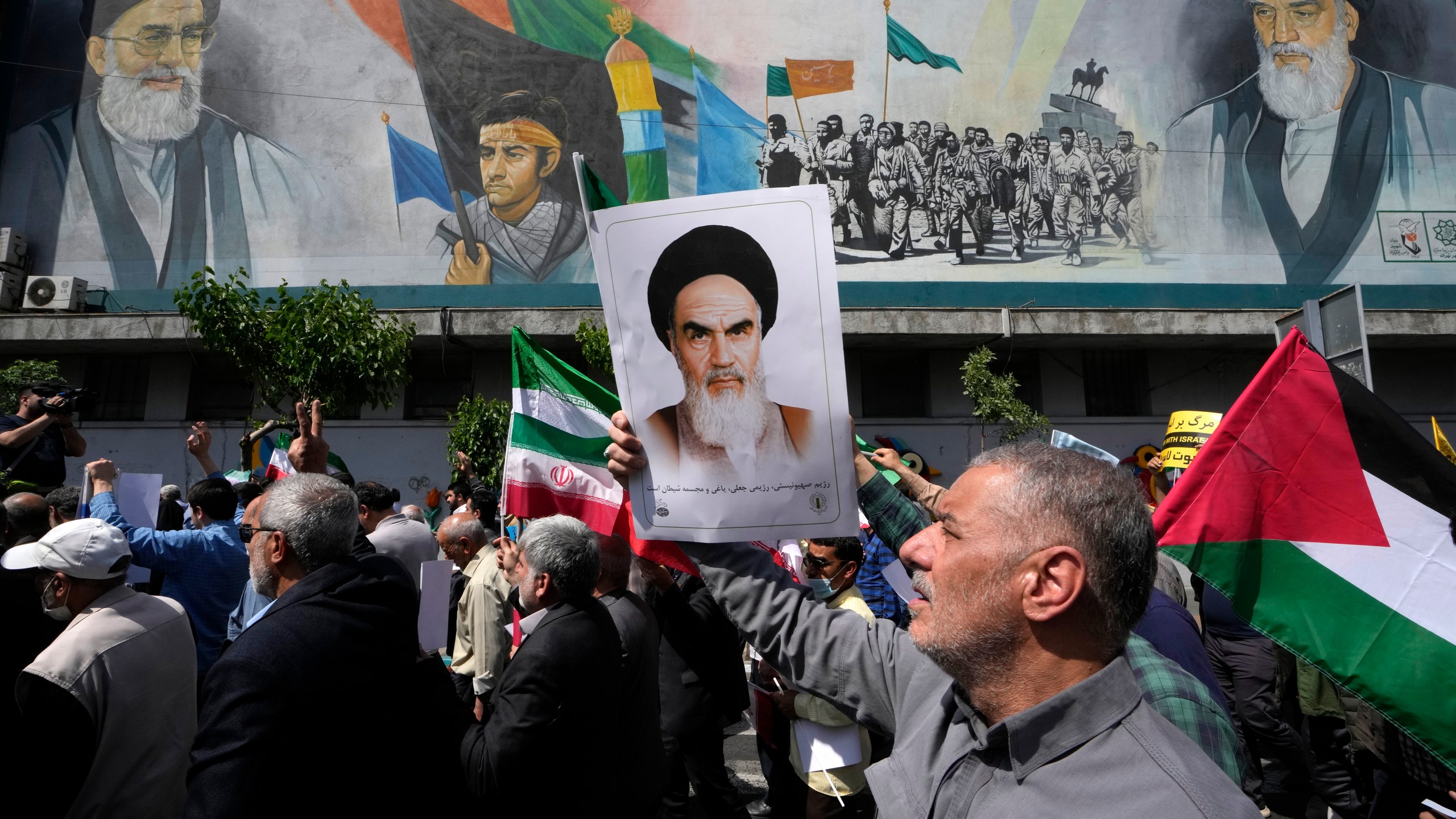 FILE - Iranian worshippers walk past a mural showing the late revolutionary founder Ayatollah Khomeini, right, Supreme Leader Ayatollah Ali Khamenei, left, and Basij paramilitary force, as they hold posters of Ayatollah Khomeini and Iranian and Palestinian flags in an anti-Israeli gathering after Friday prayers in Tehran, Iran, April 19, 2024. This month's unprecedented direct attacks between Iran and Israel are revealing deeper insights into both militaries. Experts say Friday's apparent precision strike by Israel deep into Iran demonstrated Israel's military dominance on almost all fronts. (AP Photo/Vahid Salemi, File)