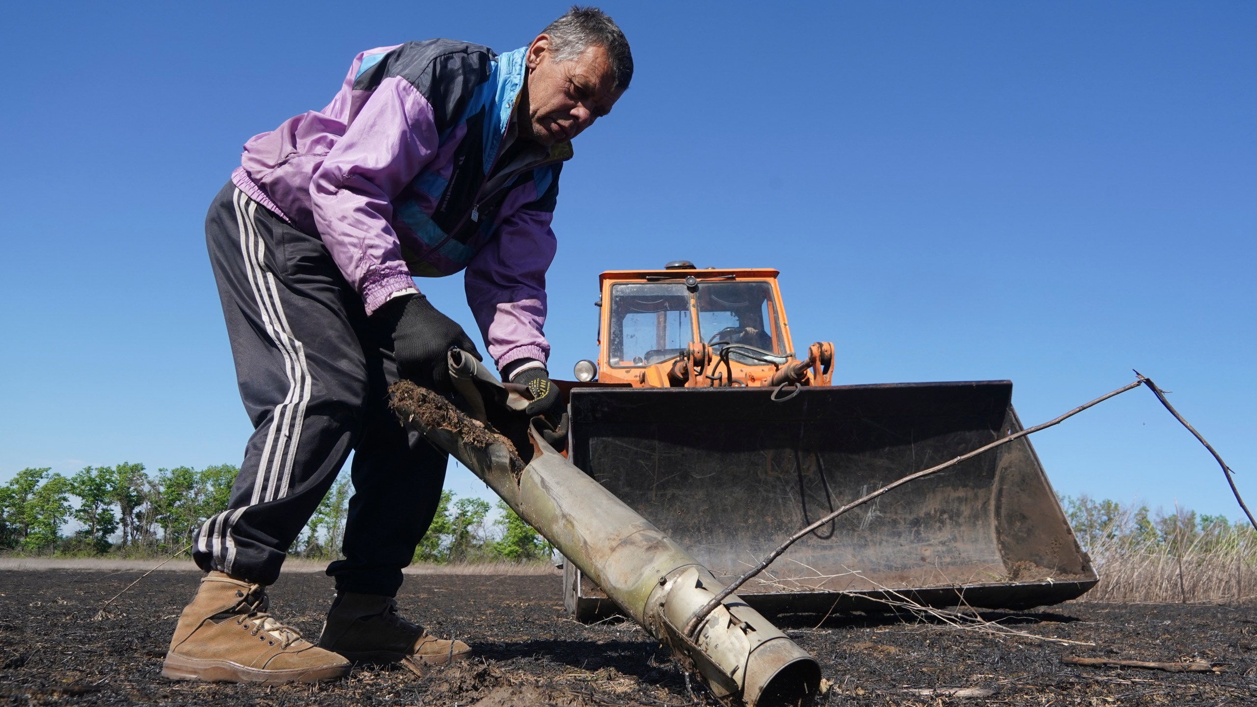 A farmer removes a fragment of a Russian missile as he works on his field in Izium, Kharkiv region, Ukraine, Saturday, April 20, 2024. (AP Photo/Andrii Marienko)