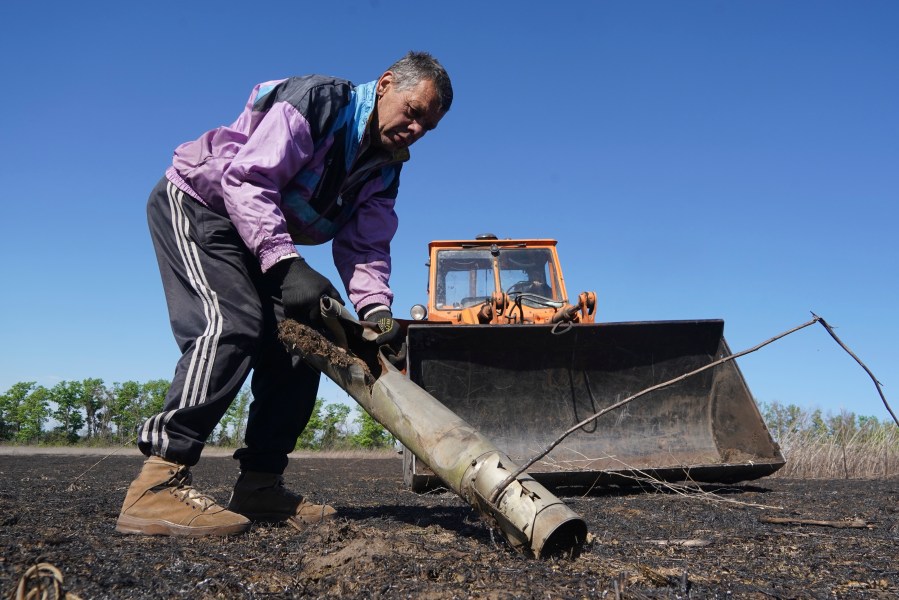 A farmer removes a fragment of a Russian missile as he works on his field in Izium, Kharkiv region, Ukraine, Saturday, April 20, 2024. (AP Photo/Andrii Marienko)