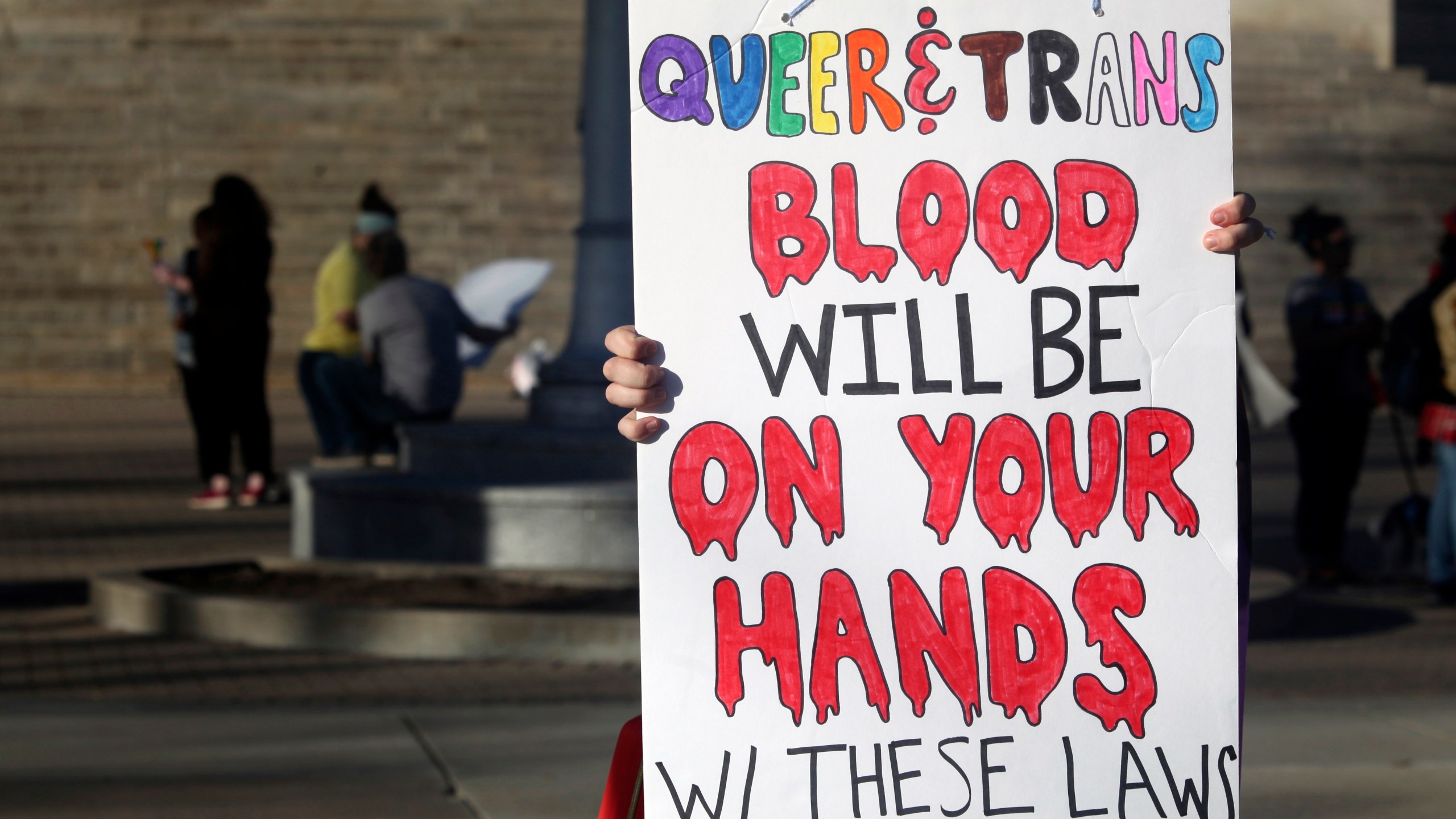 FILE - A protester outside the Kansas Statehouse holds a sign after a rally for transgender rights on the Transgender Day of Visibility, March 31, 2023, in Topeka, Kan. A new rule from President Joe Biden's administration assuring transgender students be allowed to use the school bathrooms that align with their gender identity could conflict with laws in Republican-controlled states that seek to make sure they can't. (AP Photo/John Hanna, File)