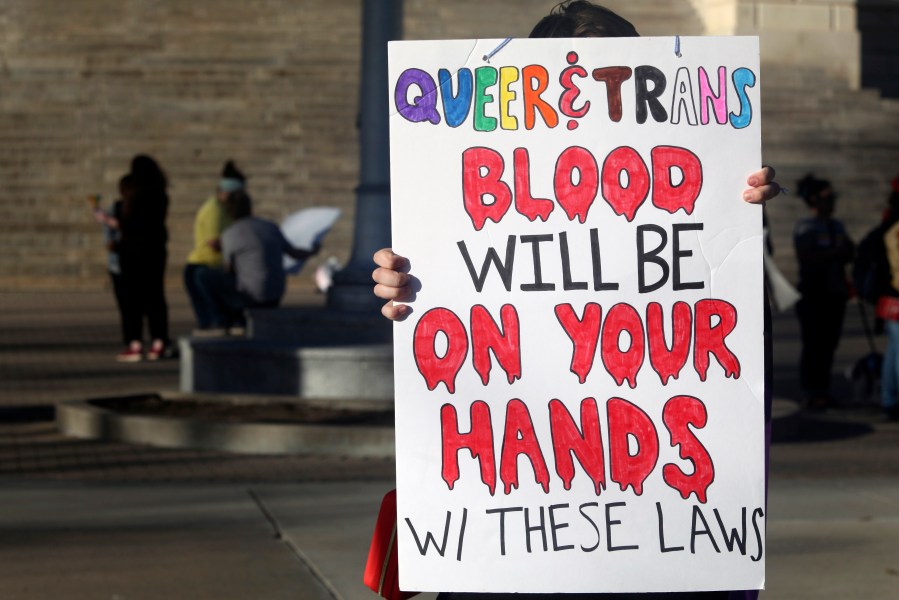 FILE - A protester outside the Kansas Statehouse holds a sign after a rally for transgender rights on the Transgender Day of Visibility, March 31, 2023, in Topeka, Kan. A new rule from President Joe Biden's administration assuring transgender students be allowed to use the school bathrooms that align with their gender identity could conflict with laws in Republican-controlled states that seek to make sure they can't. (AP Photo/John Hanna, File)