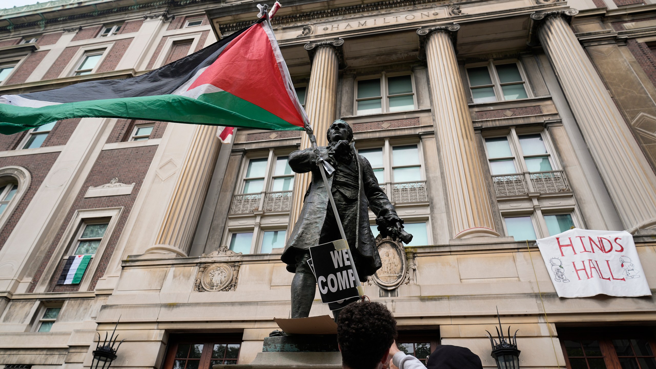 A student protester parades a Palestinian flag outside the entrance to Hamilton Hall on the campus of Columbia University, Tuesday, April 30, 2024, in New York. Early Tuesday, dozens of protesters took over Hamilton Hall, locking arms and carrying furniture and metal barricades to the building. Columbia responded by restricting access to campus. (AP Photo/Mary Altaffer, Pool)