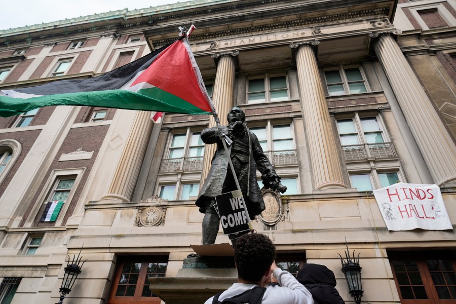 A student protester parades a Palestinian flag outside the entrance to Hamilton Hall on the campus of Columbia University, Tuesday, April 30, 2024, in New York. Early Tuesday, dozens of protesters took over Hamilton Hall, locking arms and carrying furniture and metal barricades to the building. Columbia responded by restricting access to campus. (AP Photo/Mary Altaffer, Pool)