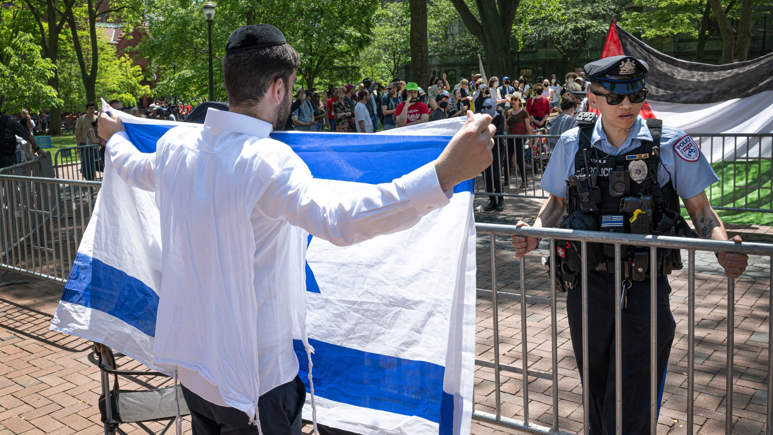 A pro-Israel supporter waves the Israeli flag in front of a police officer and a pro-Palestinian camp at the University of Pennsylvania encampment Thursday, May 2, 2024, in Philadelphia. (Jose F. Moreno/The Philadelphia Inquirer via AP)