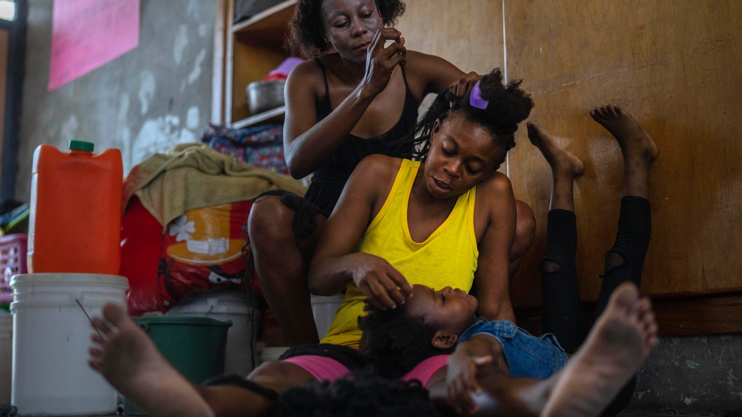 A child rests her head on the lap of her mother as she gets her hair done, at a school turned into a makeshift shelter for people displaced by gang violence, in Port-au-Prince, Haiti, Wednesday, May 8, 2024. (AP Photo/Ramon Espinosa)