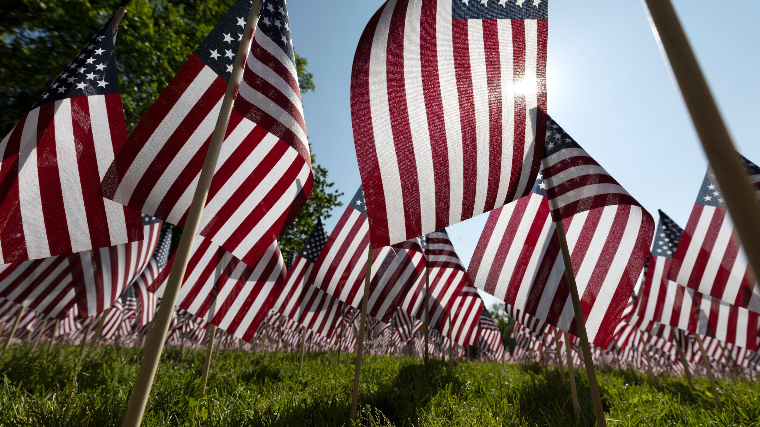 FILE - The sun shines through the flags in the Memorial Day Flag Garden on Boston Common, May 27, 2023, in Boston. Memorial Day is supposed to be about mourning the nation’s fallen service members. But it’s come to anchor the unofficial start of summer and retail discounts. (AP Photo/Michael Dwyer, file)