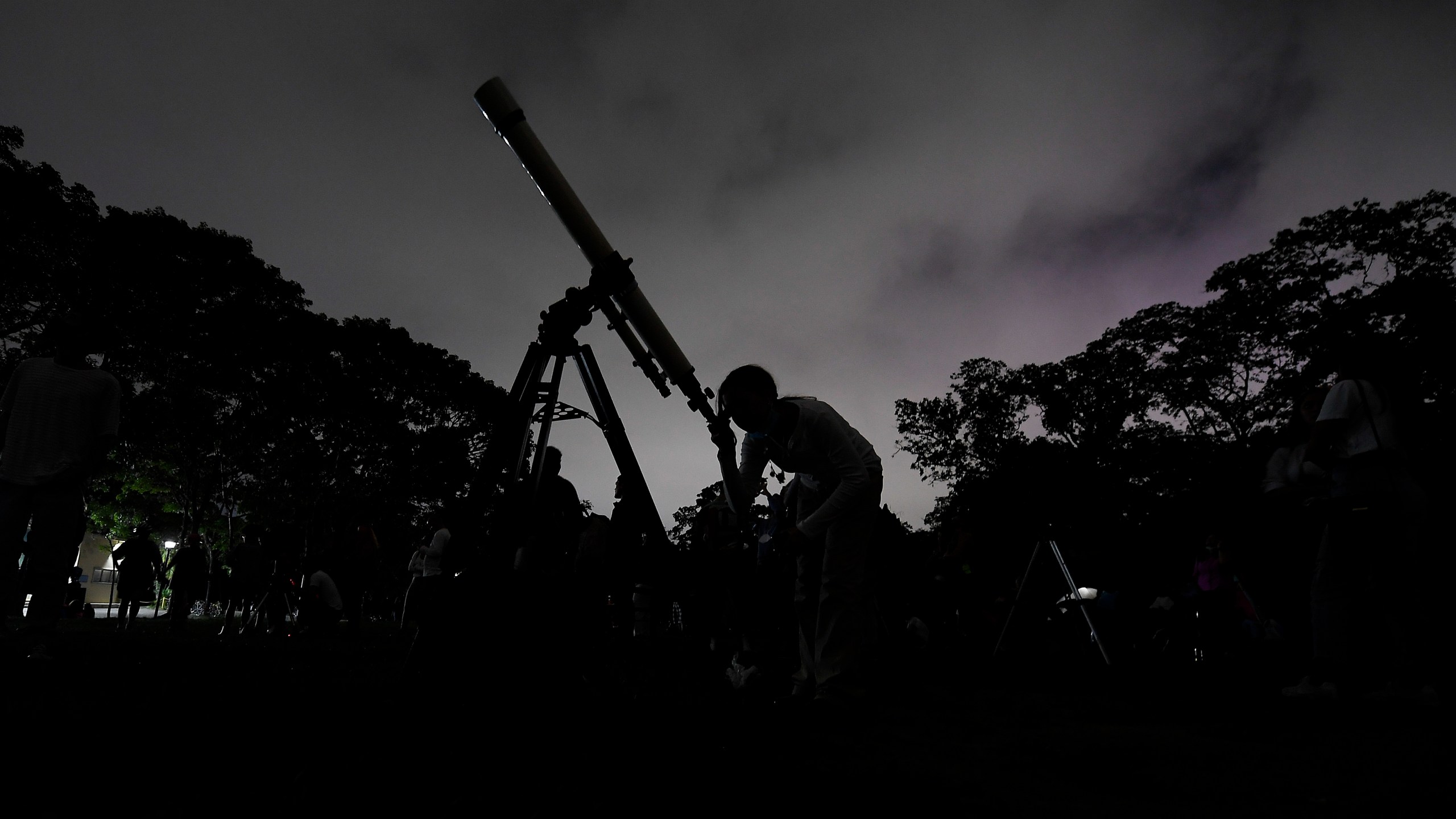 FILE - A girl looks at the moon through a telescope in Caracas, Venezuela, on Sunday, May 15, 2022. Six planets will line up in the early morning sky on June 3, 2024 but most won't be visible to the naked eye. A planetary parade happens relatively often when several planets align on the right side of the sun, making them visible across a narrow band of our sky. (AP Photo/Matias Delacroix)