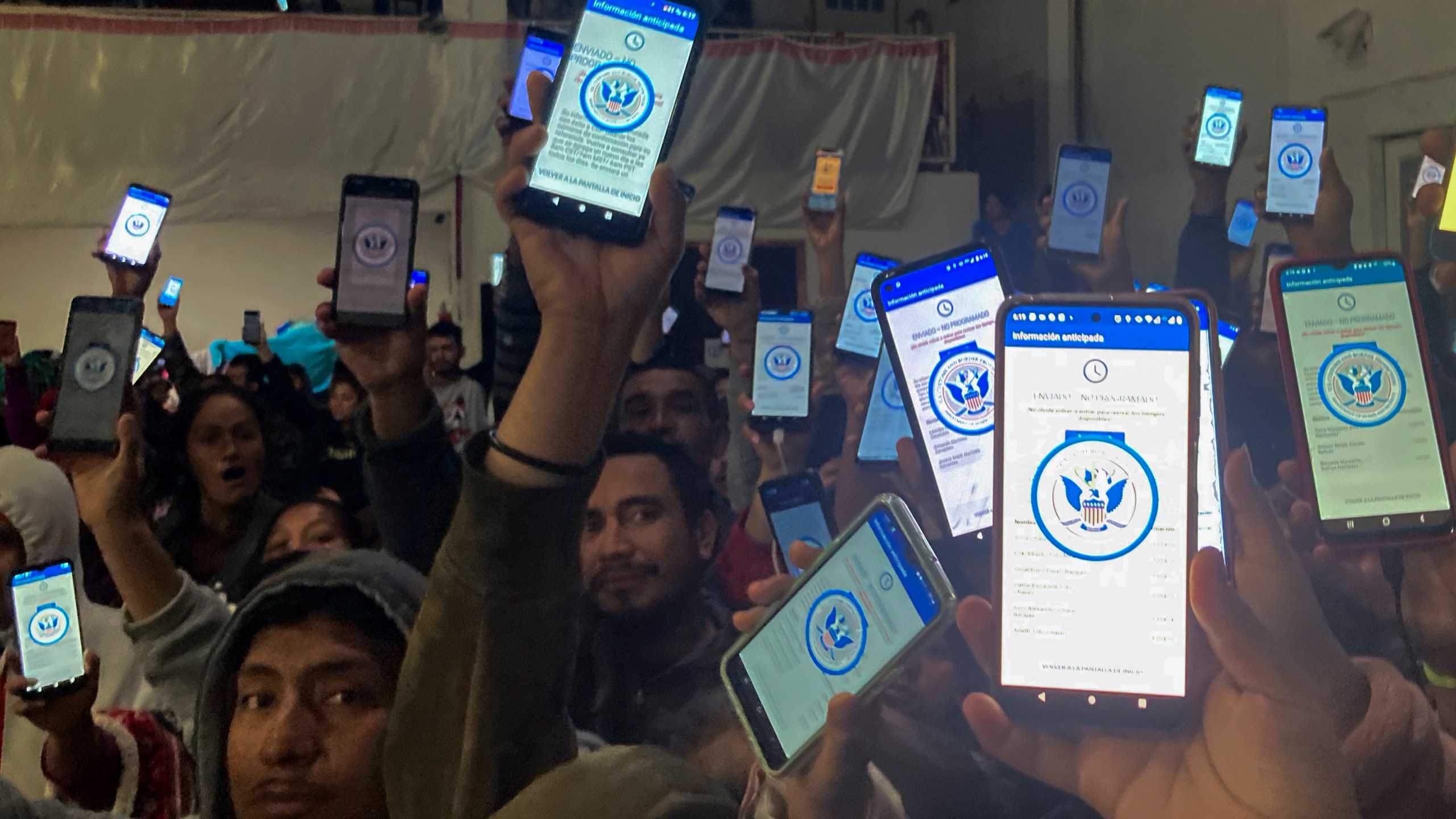 Migrants holding up phones with the CBP One app.