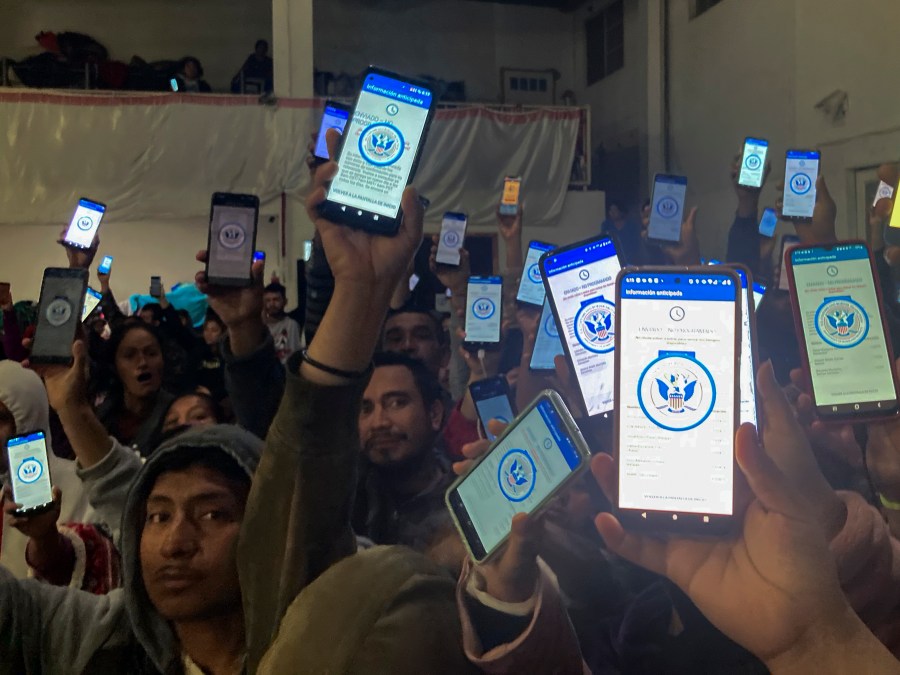 Migrants holding up phones with the CBP One app.