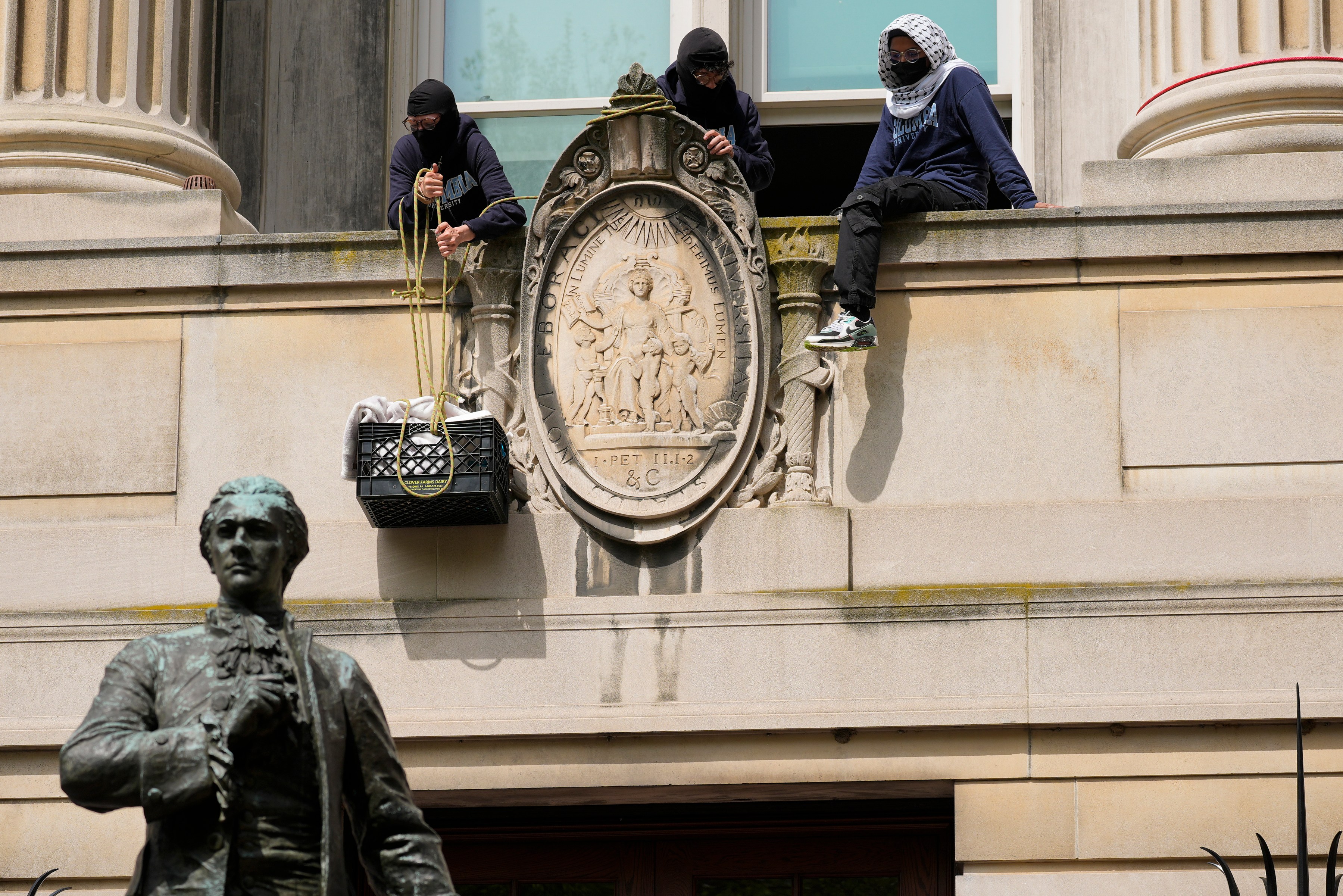 Three people in masks pulling a crate up the side of the building with ropes.