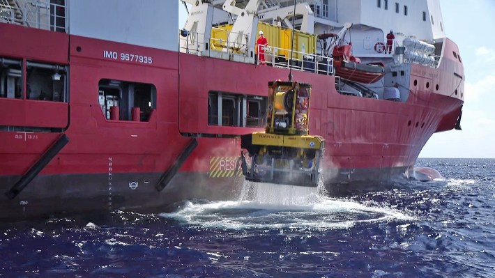 A container being raised out of the ocean near a ship.