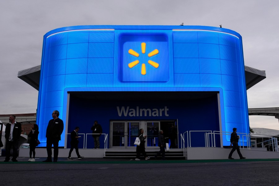 FILE - People walk by the Walmart booth during the CES tech show Tuesday, Jan. 9, 2024, in Las Vegas. Walmart is offering new perks for its hourly workers. They include a new bonus plan as well as opportunities to move into skilled trade jobs within the company. (AP Photo/John Locher, file)