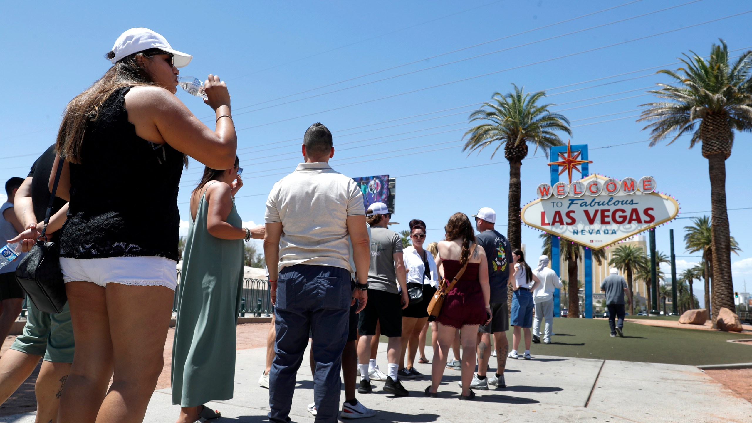 Sofia Ramirez, left, of Mexico drinks water as she waits in line to take a photo at the Welcome to Fabulous Las Vegas sign in Las Vegas Thursday, June 6, 2024. (Steve Marcus/Las Vegas Sun via AP)