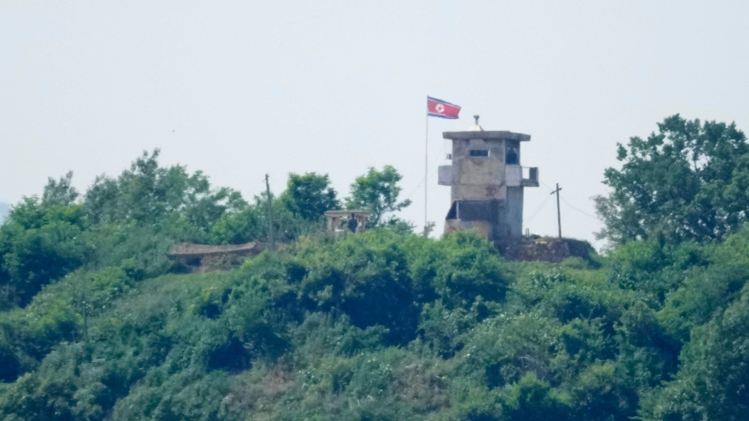 North Korean soldiers stand near their military guard post as a North Korean flag flutters in the wind, seen from Paju, South Korea, Sunday, June 9, 2024. South Korean soldiers fired warning shots after North Korean troops briefly violated the tense border earlier this week, South Korea's military said Tuesday, as the rivals are embroiled in Cold War-style campaigns like balloon launches and propaganda broadcasts. (AP Photo/Lee Jin-man)