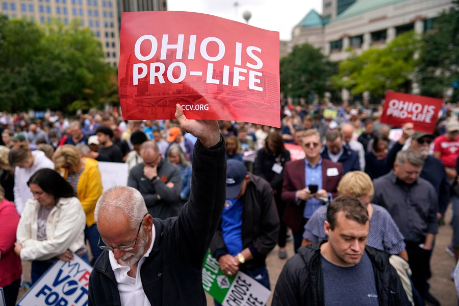 FILE - Paul Meacham holds high a sign that reads "Ohio is pro-life" as the crowd prays during the Ohio March for Life rally at the Ohio State House in Columbus, Ohio, Friday, Oct. 6, 2023. Two years after the U.S. Supreme Court ended a nationwide right to abortion, travel and pills have become big parts of the issue. (AP Photo/Carolyn Kaster, File)