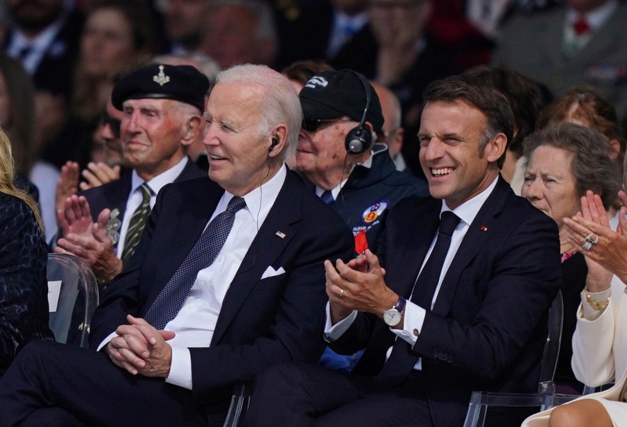 FILE - President Joe Biden, left, and President of France Emmanuel Macron attend the official international ceremony to mark the 80th anniversary of D-Day, at Omaha Beach in Saint-Laurent-sur-Mer, Normandy, France, June 6, 2024. Biden's simple act of sitting down at the D-Day event gained attention as social media users shared a shortened version of the clip to falsely claim he was reaching for a nonexistent chair. Republicans have shared a spate of misleading, out-of-context videos to fuel a narrative that President Joe Biden is mentally and physically unfit for office. These widespread misleading videos show how the reach of social media and real concerns about Biden's age have made the tactic especially powerful in 2024. (Jordan Pettitt/Pool Photo via AP, File)