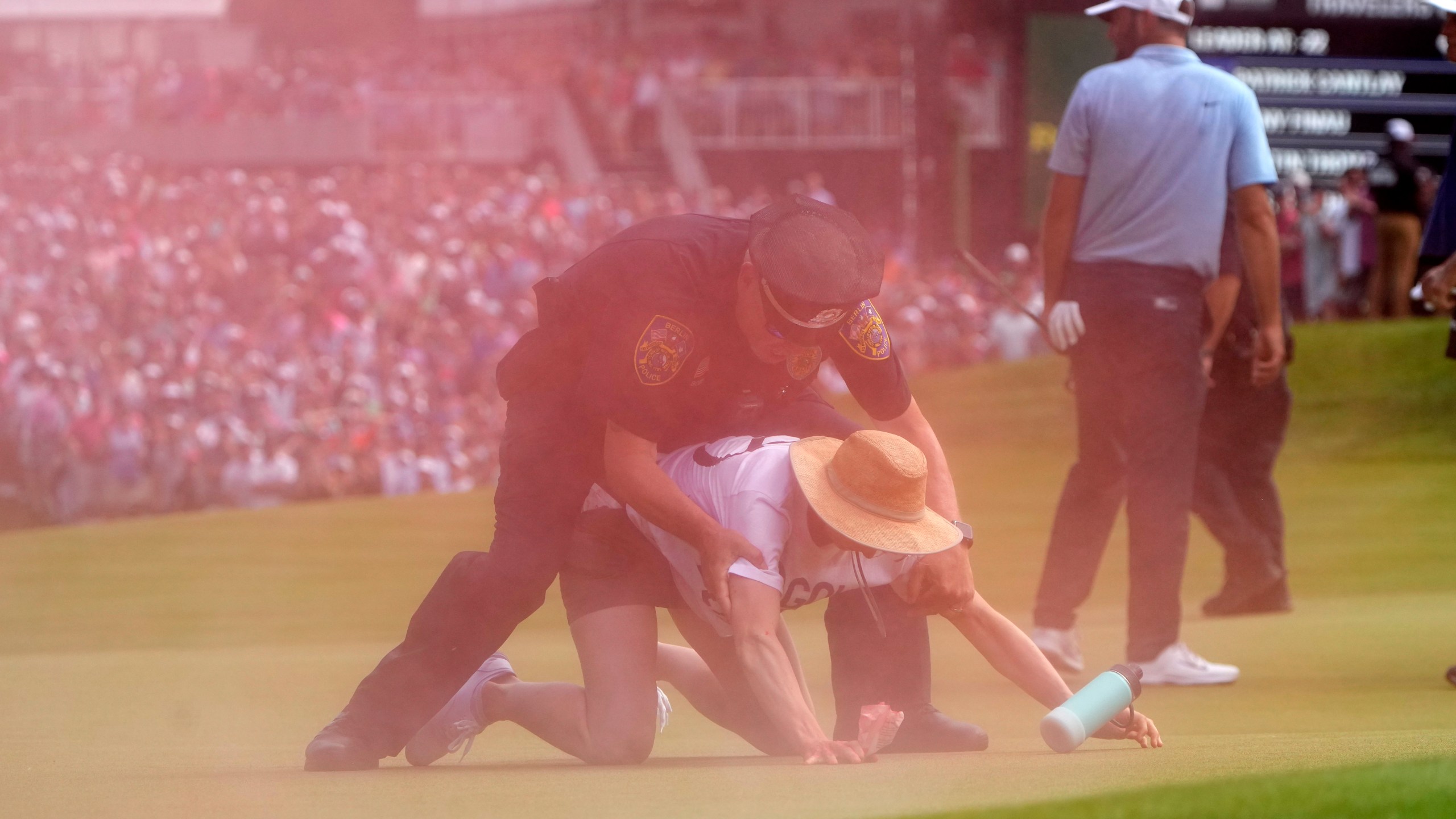 A protester is taken into custody after he ran onto the course as Scottie Scheffler, right, walks away on the 18th hole during the final round of the Travelers Championship golf tournament at TPC River Highlands, Sunday, June 23, 2024, in Cromwell, Conn. (AP Photo/Seth Wenig)