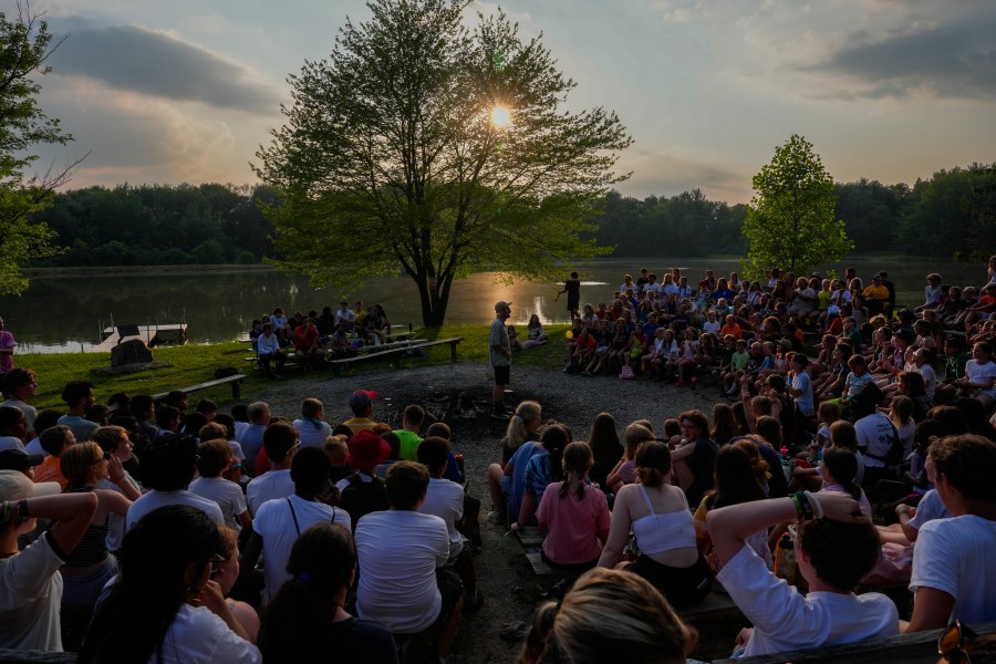 Counselors perform a camp song during closing campfire, Thursday, June 20, 2024, at YMCA Camp Kern in Oregonia, Ohio. As the first heat wave of the season ripples across the U.S., summer camps are working to keep their children cool while still letting the kids enjoy being outside with nature. (AP Photo/Joshua A. Bickel)