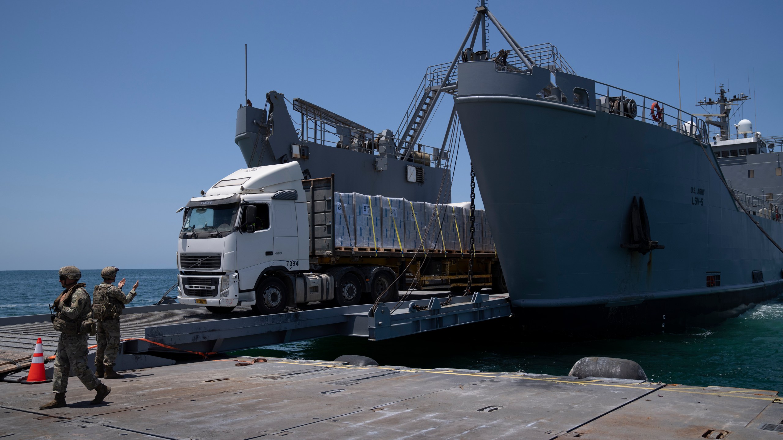 A U.S. Army soldier gestures as trucks loaded with humanitarian aid arrive at the U.S.-built floating pier Trident before reaching the beach on the coast of the Gaza Strip, Tuesday, June 25, 2024. (AP Photo/Leo Correa)