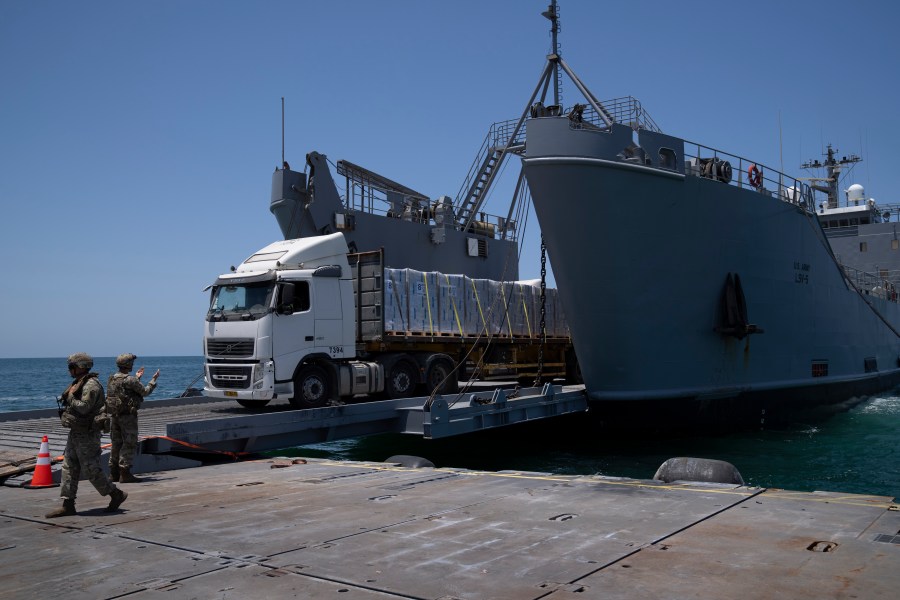 A U.S. Army soldier gestures as trucks loaded with humanitarian aid arrive at the U.S.-built floating pier Trident before reaching the beach on the coast of the Gaza Strip, Tuesday, June 25, 2024. (AP Photo/Leo Correa)