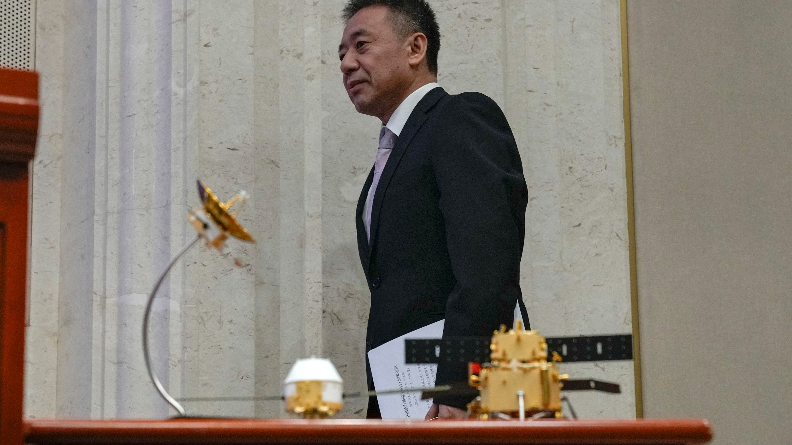 Bian Zhigang, Deputy Director of the China National Space Administration walks by Chang'e 6 probe models as he arrives for a press conference at the State Council Information Office in Beijing, Thursday, June 27, 2024. China's space officials said Thursday they welcomed scientists from across the world to apply to study the lunar rock samples the Chang'e 6 probe brought back to earth in a historic mission, but noted there were limits to that cooperation, specifically with the U.S. (AP Photo/Andy Wong)