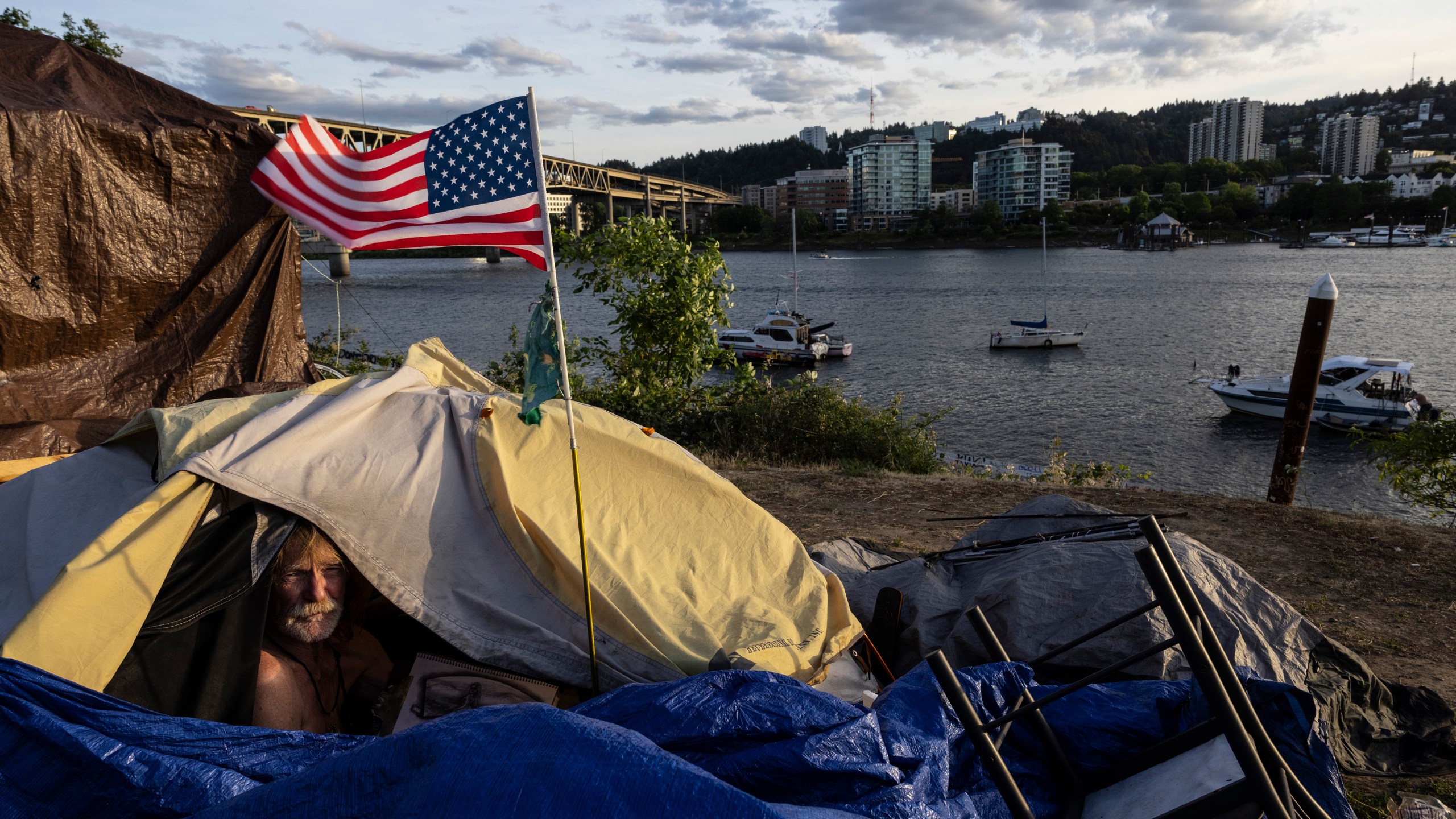 FILE - Frank, a homeless man, sits in his tent with a river view, June 5, 2021, in Portland, Ore. The Supreme Court ruled on Friday, June 28, 2024, that cities can enforce bans on homeless people sleeping outdoors in West Coast areas where shelter space is lacking. (AP Photo/Paula Bronstein, File)