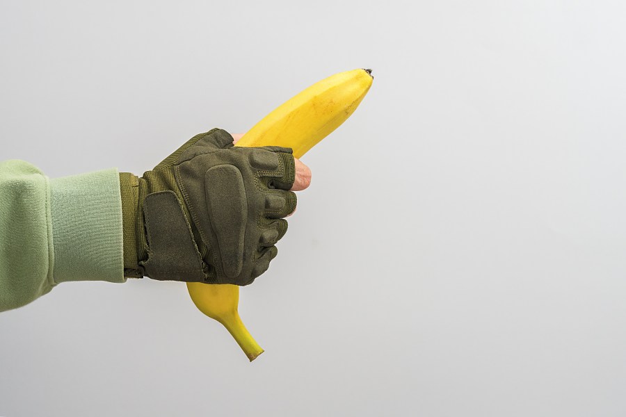 A man's military hand holds a banana on a gray background.