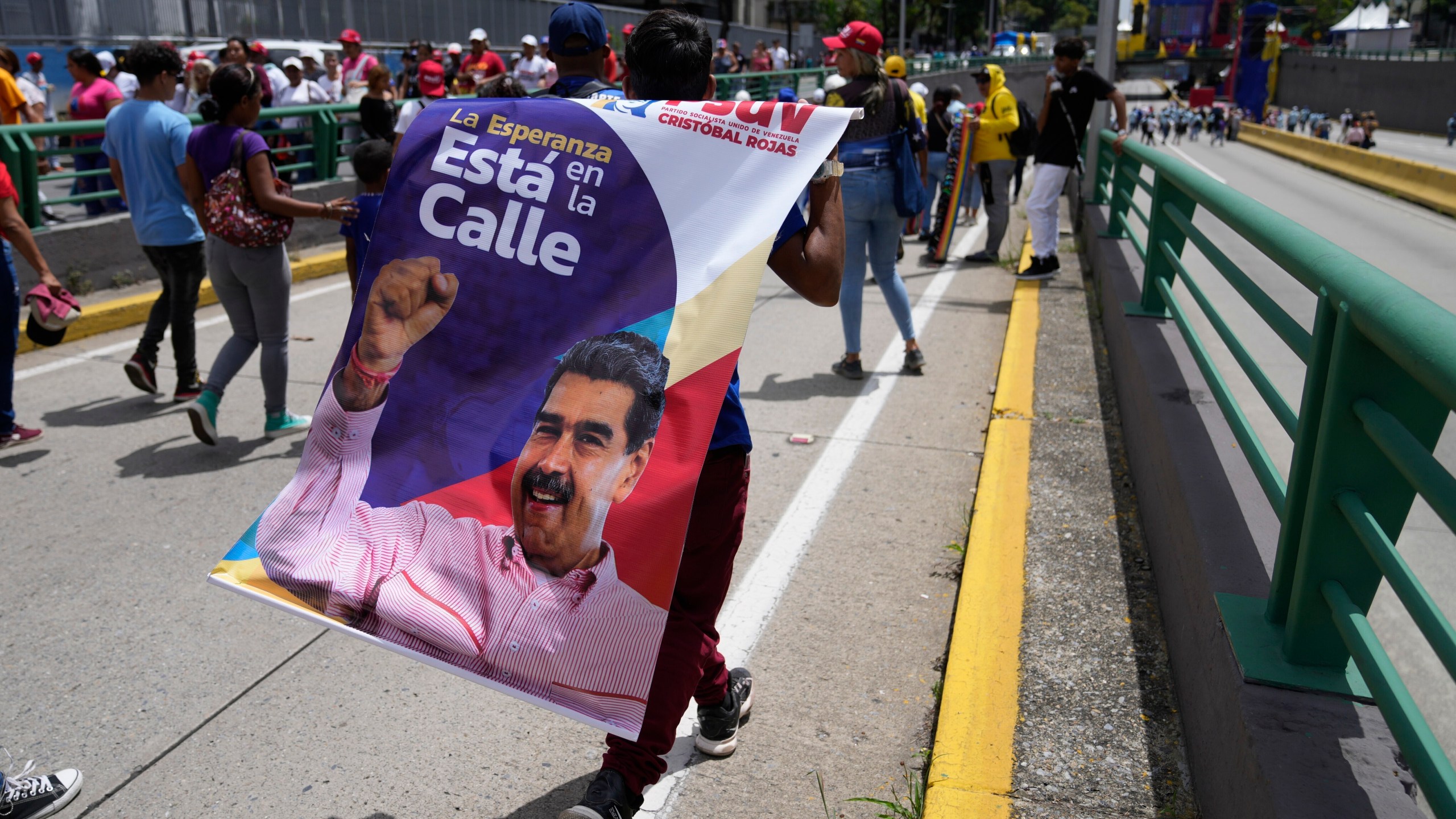 A supporter of Venezuelan president Nicolas Maduro carries a banner with his image ahead of a rally marking the beginning of official campaigns for the July 28 presidential election in Caracas, Venezuela, Thursday, July 4, 2024. (AP Photo/Ariana Cubillos)