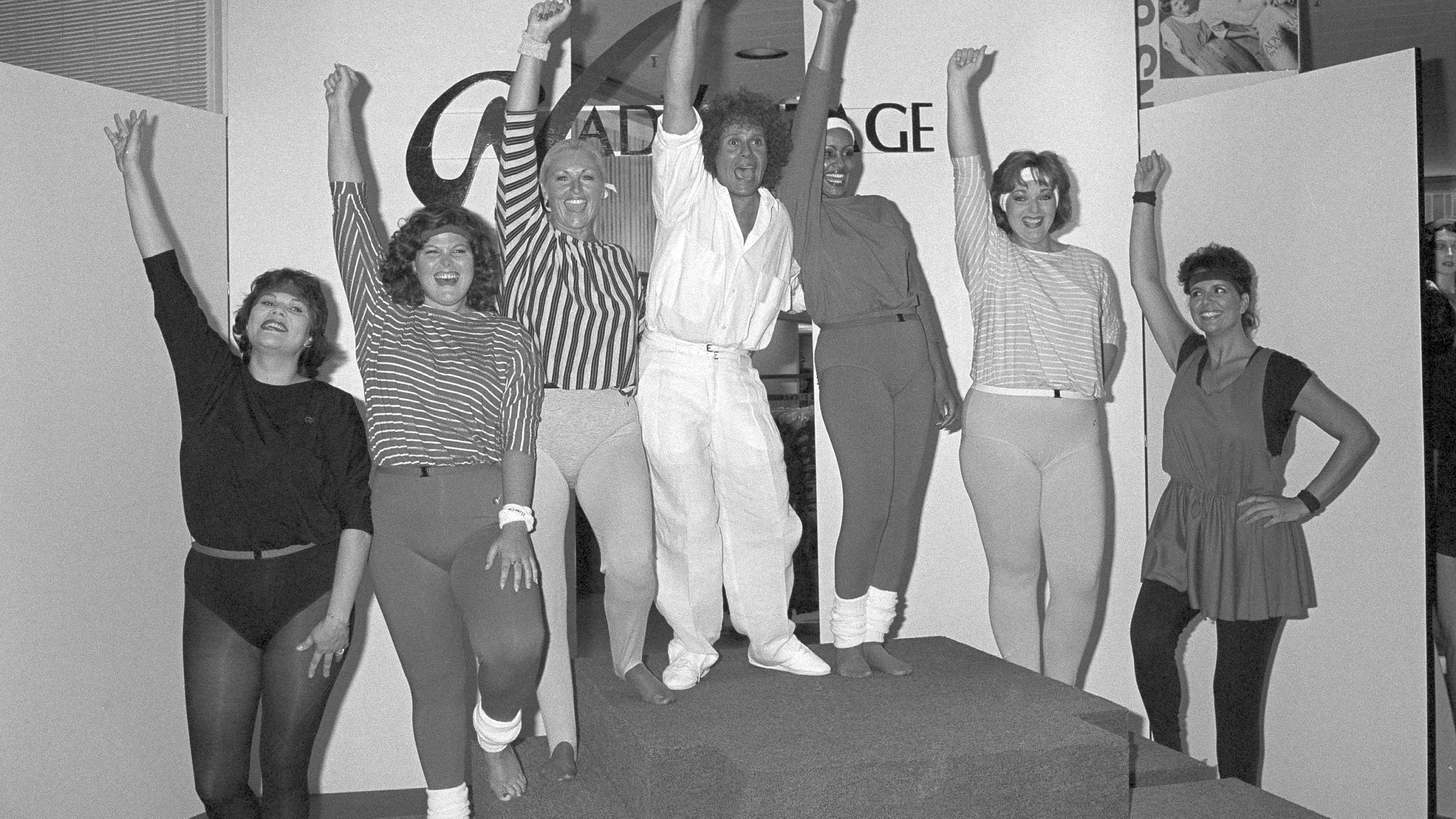 FILE - Richard Simmons, center, is surrounded by models displaying his new line of "Advantage" clothing exclusively for women sized 16-44 as he gives a hoot in Los Angeles for big and beautiful women, Aug. 2, 1984. "You should feel great no matter what size," says Simmons. Simmons, a fitness guru who urged the overweight to exercise and eat better, died Saturday, July 13, 2024, at the age of 76. (AP Photo/Mark Avery, File)