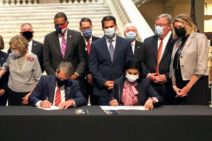 FILE - Georgia Gov. Brian Kemp, left, and Centers for Medicare and Medicaid Services Administrator Seema Verma, right, sign healthcare waivers at the state Capitol in Atlanta, Oct. 15, 2020. Pathways to Coverage launched last July and is the only Medicaid plan in the country that requires beneficiaries to work or engage in other activities to get coverage. As of June, it had about 4,300 members. (AP Photo/Jeff Amy, File)