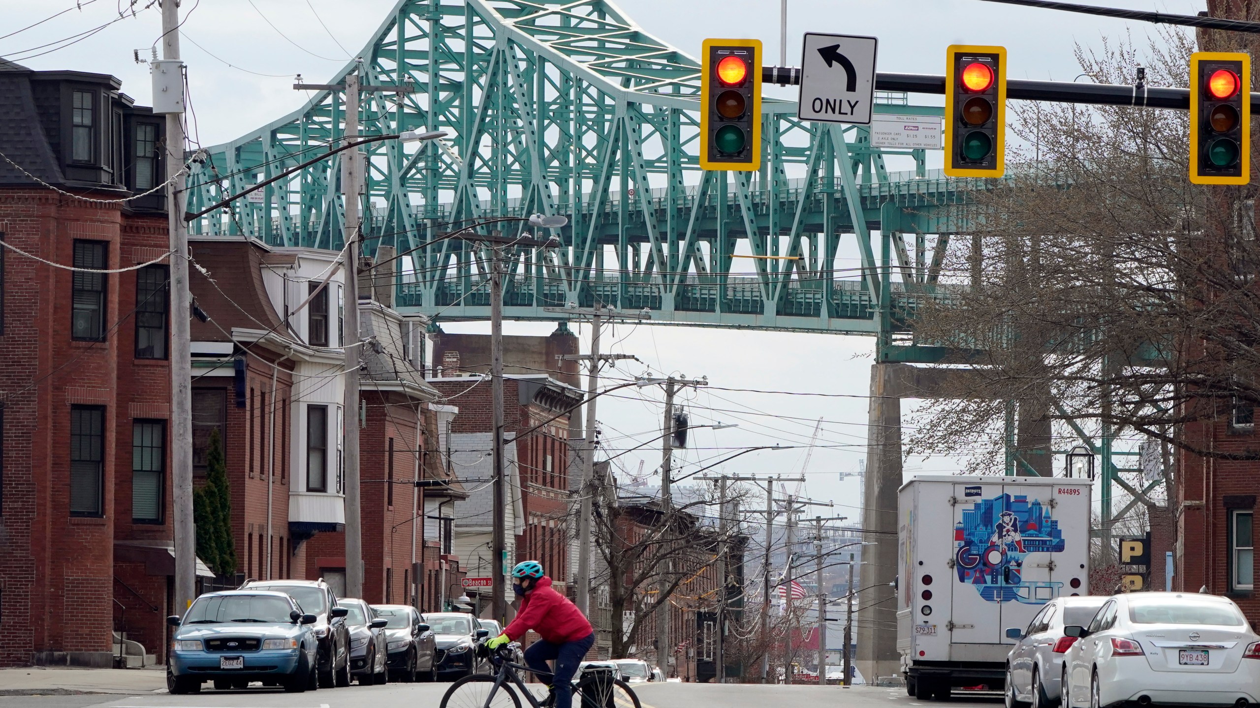 FILE - A cyclist rides along a street near the Tobin Memorial Bridge, background, in Chelsea, Mass., on Wednesday, March 31, 2021. After nearly 1,750 low-income people in the Boston suburb won a lottery to receive monthly stipends from the city from November 2020 to August 2021, researchers found that winners visited emergency departments significantly less than people who did not receive the monthly payments. (AP Photo/Steven Senne, File)