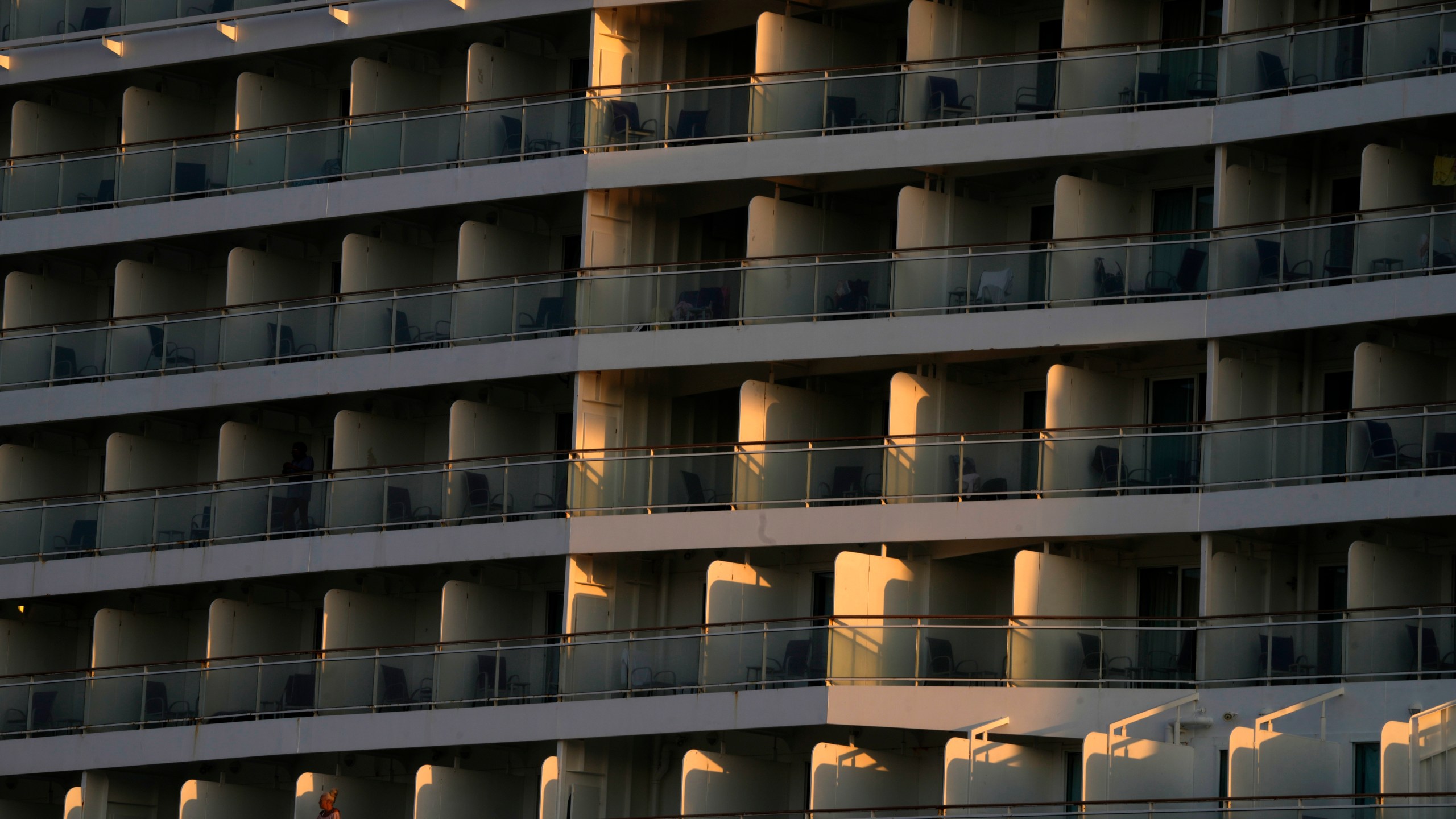 A woman, bottom left, stands on the balcony of a cruise ship which is docked at Athens' port city of Piraeus, as the sun rises on Monday, July 22, 2024. The heatwave continues in Greece, with temperatures hovering at 40 degrees Celsius (104 Fahrenheit) in several places, but the meteorologists expecting to slight drop from tomorrow. (AP Photo/Thanassis Stavrakis)