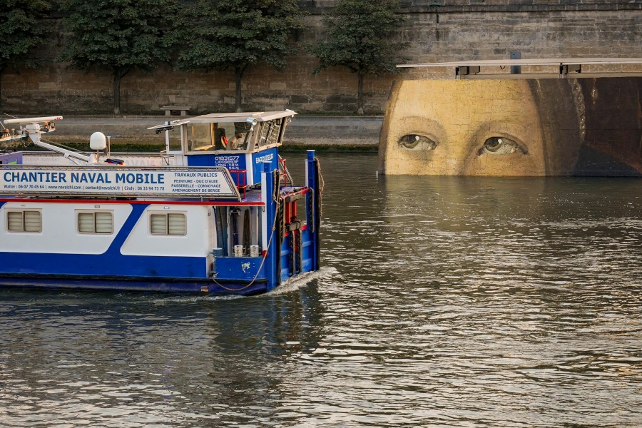 A ship sails past reproductions of artworks decorating the banks of the River Seineat the 2024 Summer Olympics, Tuesday, July 30, 2024, in Paris, France. The men's Olympic triathlon has been postponed over concerns about water quality in Paris' Seine River, where the swimming portion of the race was supposed to take place. (AP Photo/ Dar Yasin)