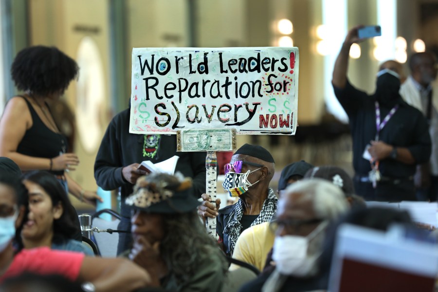 An 80-year-old man holds up a sign urging world leaders to provide reparations in 2022.