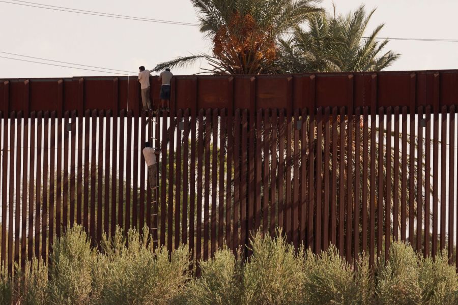 Migrants use a rope ladder to illegally climb over the US Border Wall