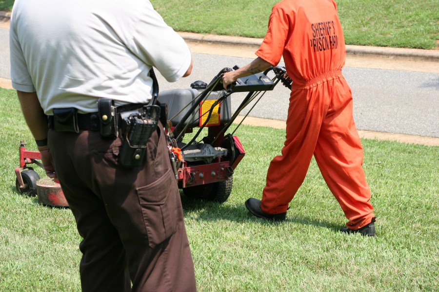 Prisoner working while law enforcement officer keeps watch.