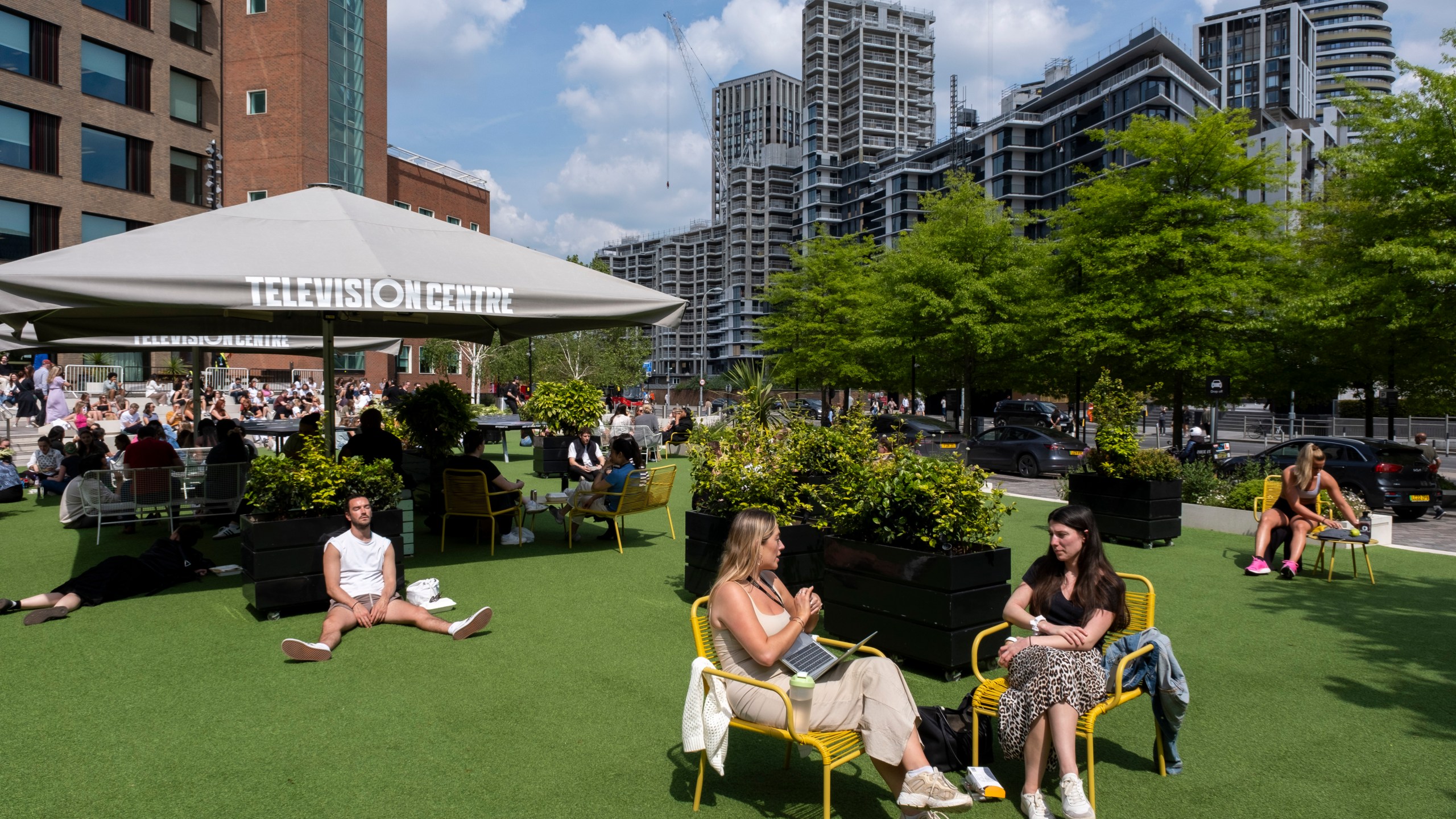 Young workers hanging out on the fake grass in the sunshine outside BBC Television Centre