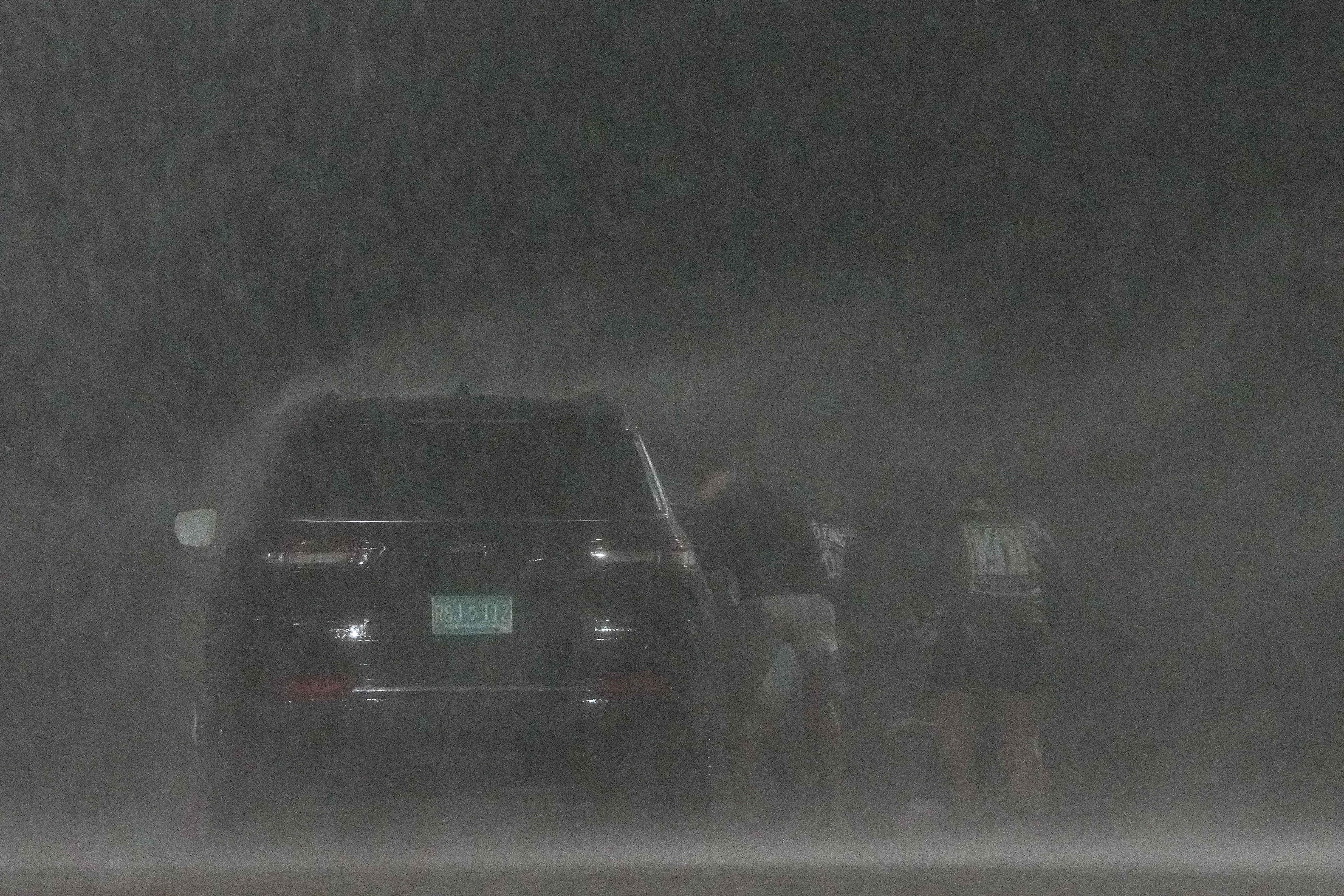 A group of people hide behind a car to shield themselves from wind and rain from Hurricane Beryl.