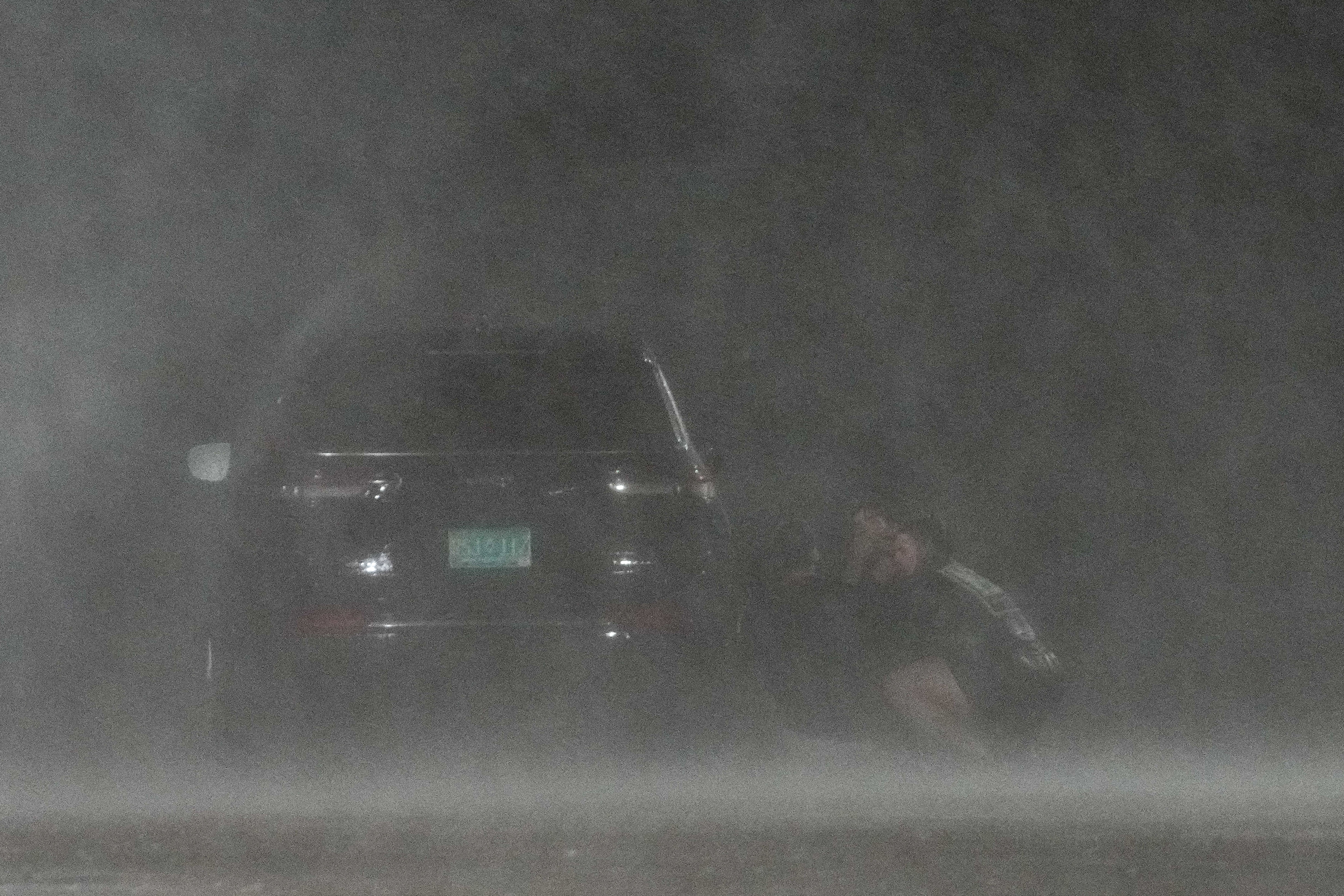 A group of people hide behind a car to shield themselves from wind and rain from Hurricane Beryl.