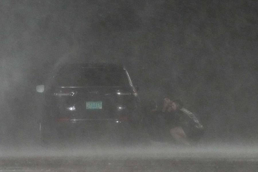 A group of people hide behind a car to shield themselves from wind and rain from Hurricane Beryl. 