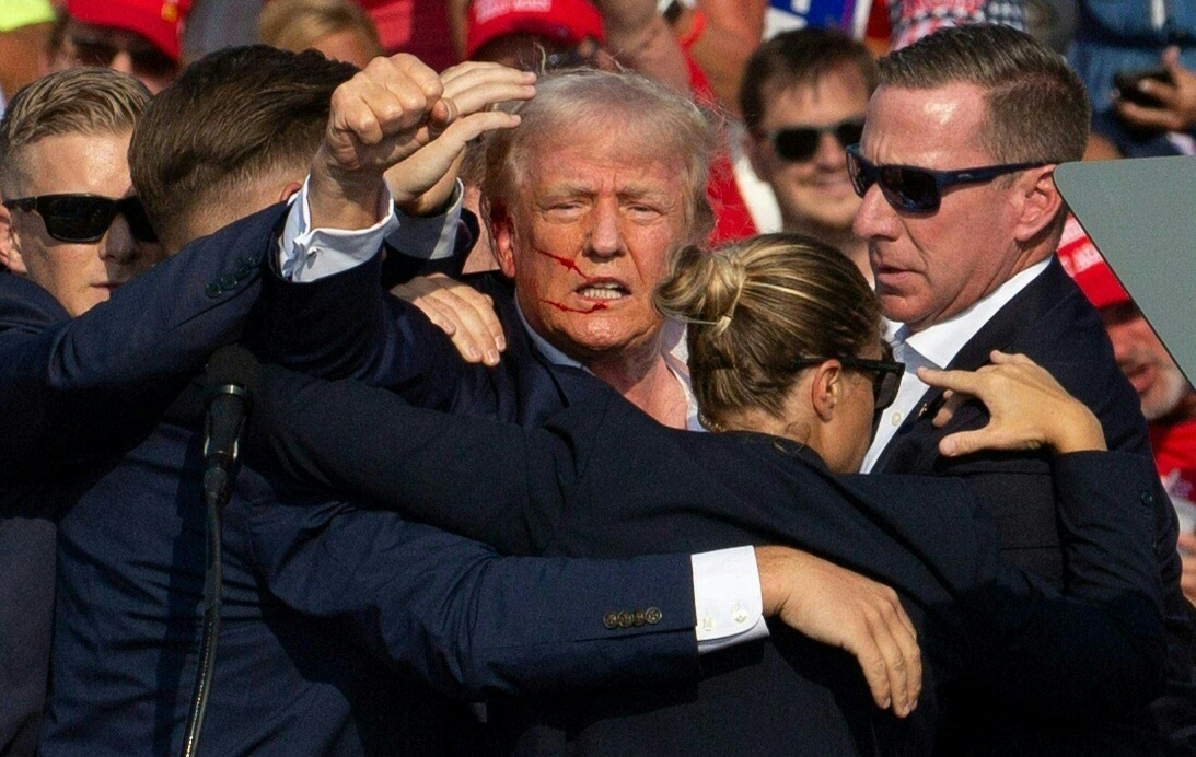 Donald Trump is seen with blood on his face surrounded by Secret Service agents following an assassination attempt.