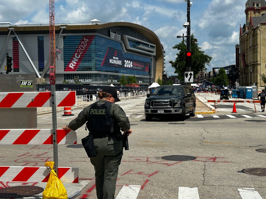 A police officer in a bulletproof vest and a police vehicle block traffic between two crosswalks.