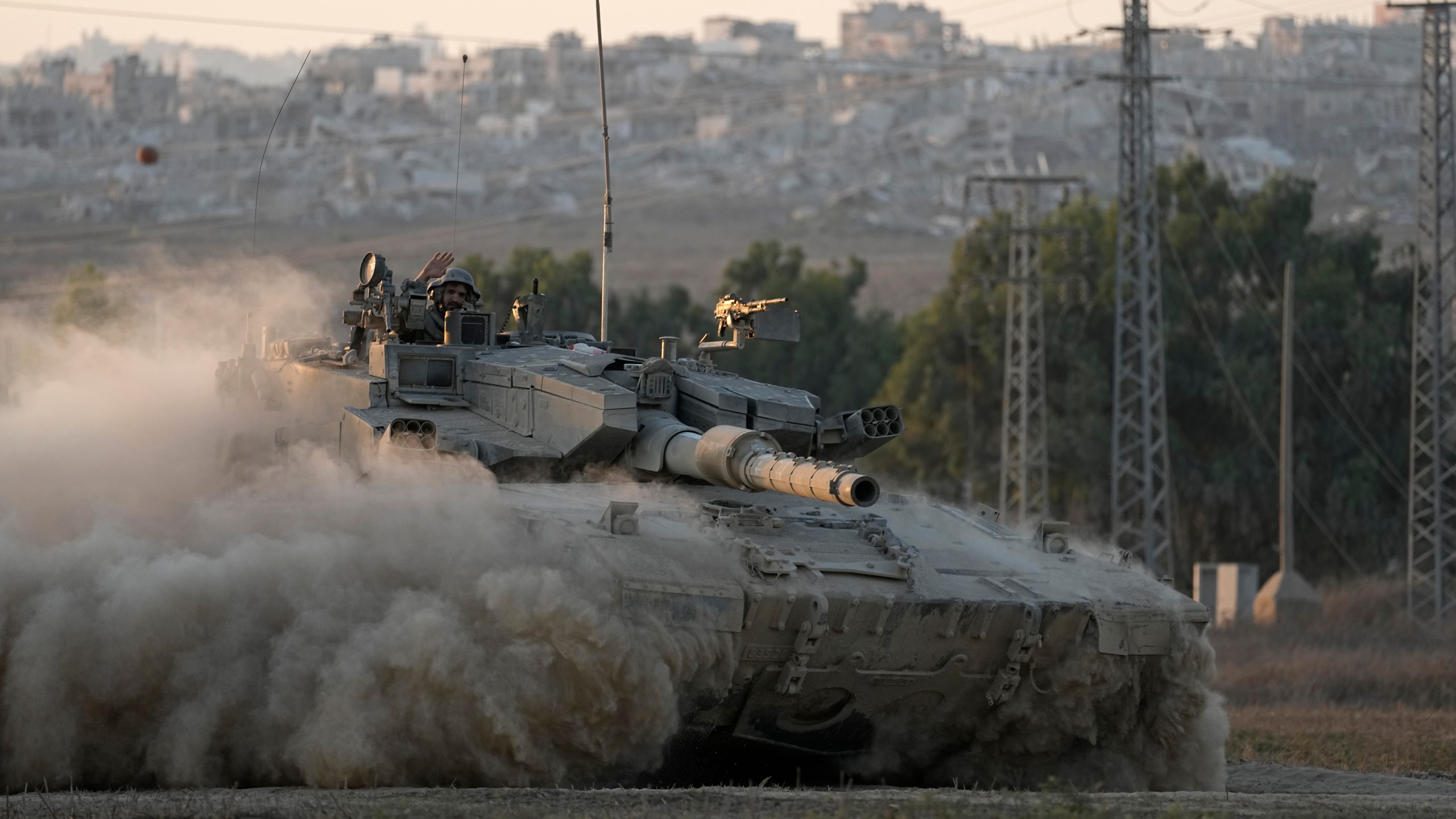 With destroyed buildings in the Gaza Strip behind him, an Israeli soldier waves from a tank, near the Israel-Gaza border in southern Israel, Thursday, Aug. 1, 2024. (AP Photo/Tsafrir Abayov)